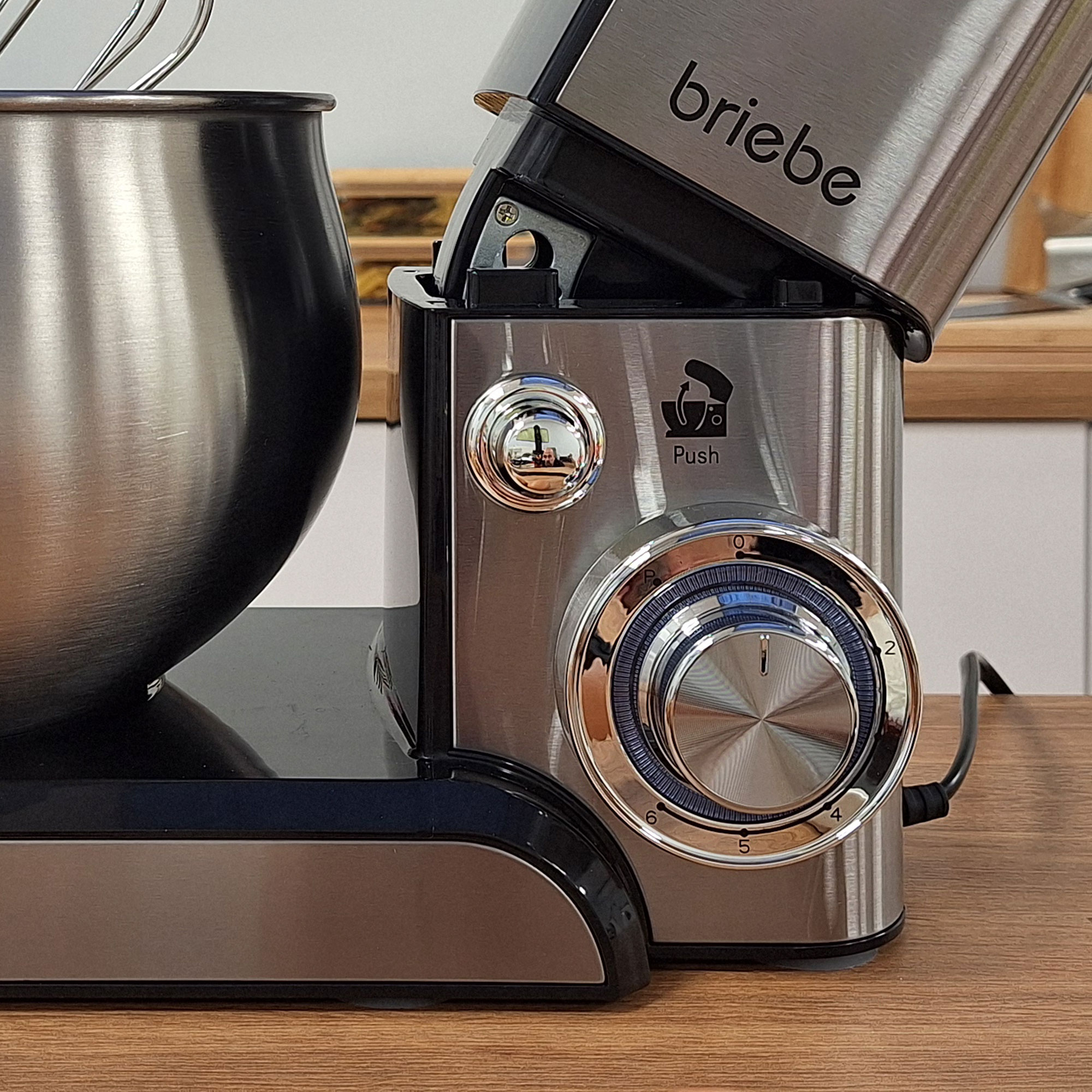 Edelstahl-Küchenmaschine mit schwarzer Schüssel und silbernen Aufsätzen auf Holz.
