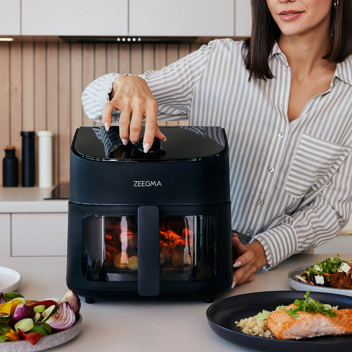 Kobieta używa czarnej frytkownicy Zeegma na blacie. Warzywa i jedzenie są umieszczone na blacie.