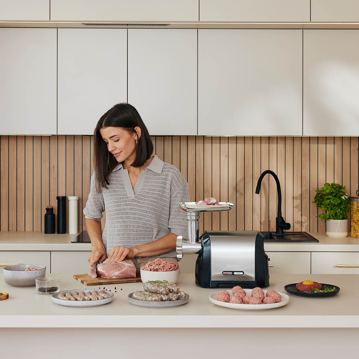 Kobieta przygotowująca mięso. Otoczenie kuchni, maszynka do mięsa, różne talerze z jedzeniem.