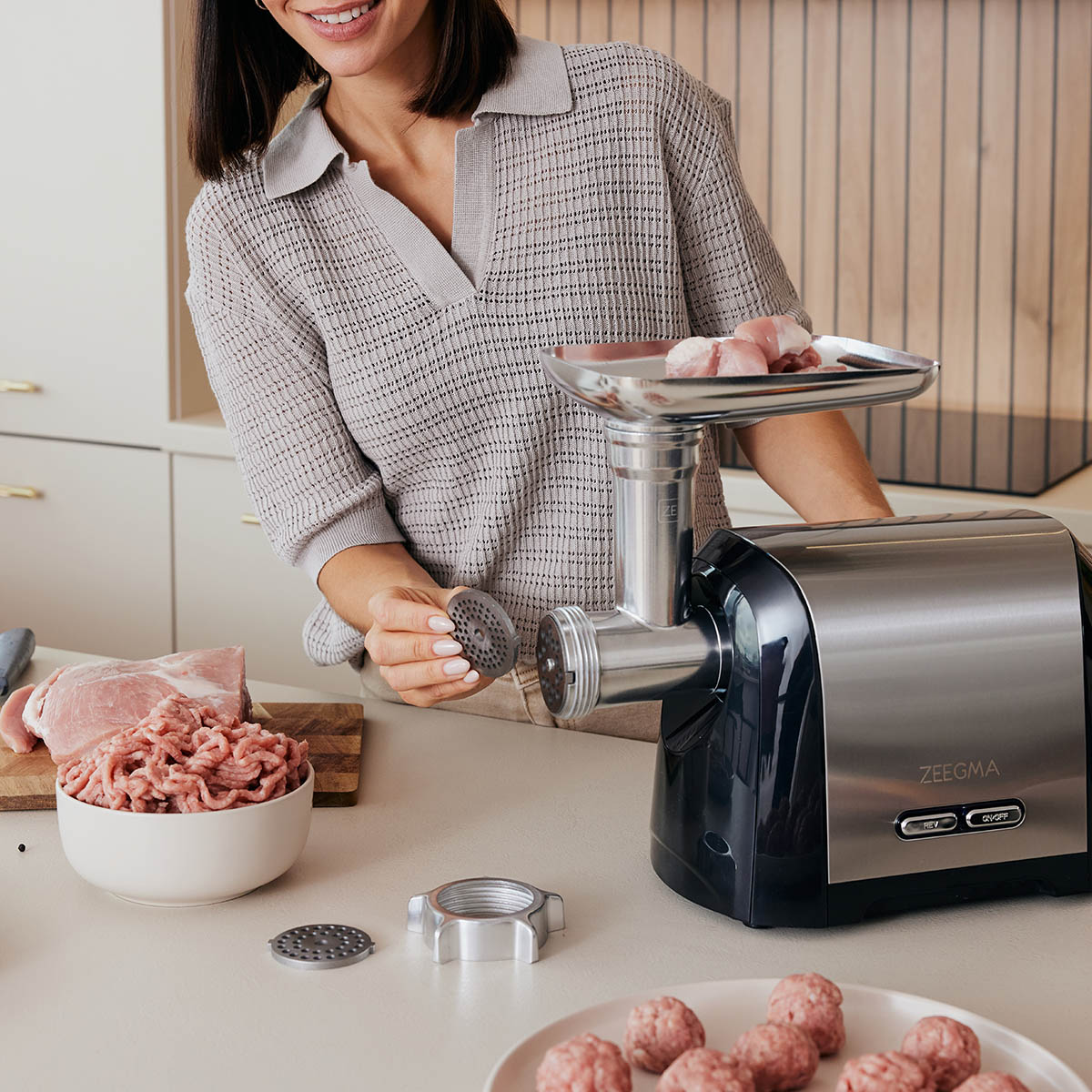 Kobieta używa maszynki do mięsa. Mielone mięso w misce i inne mięso w pobliżu.