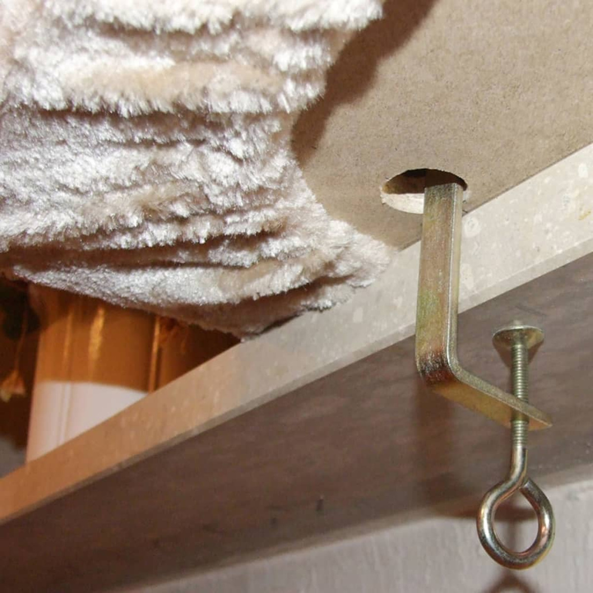 Eine Metallklemme sichert ein Regal mit einem flauschigen beigen Material darauf.