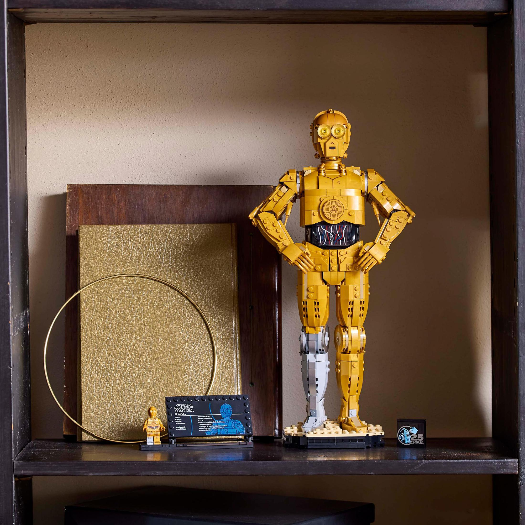 Figurka Lego C-3PO na półce z małą figurką, tabliczką znamionową i złotym pierścieniem.