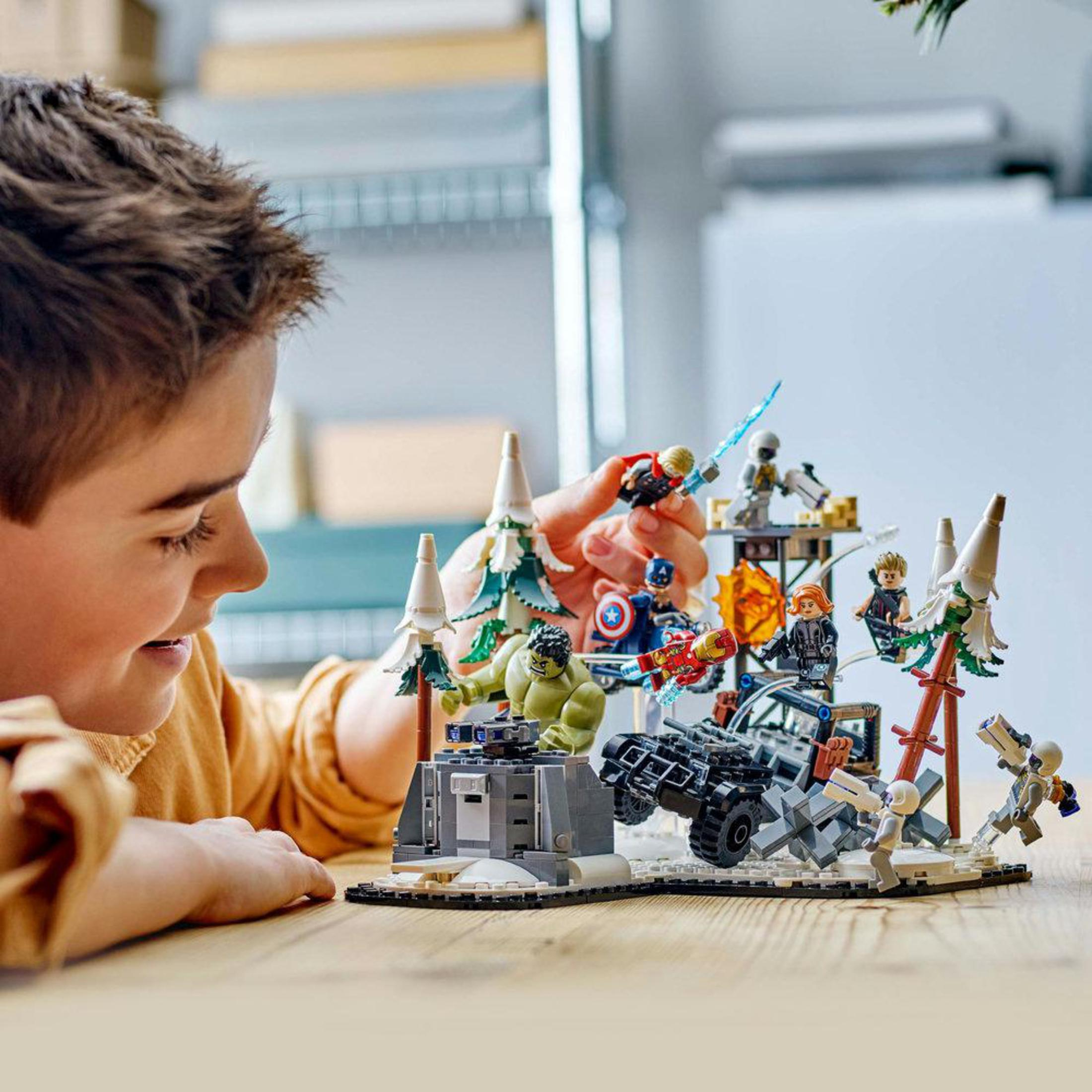 Ein Junge lächelt ein Lego-Set der Avengers an. Das Set enthält Figuren und eine Kampfszene.