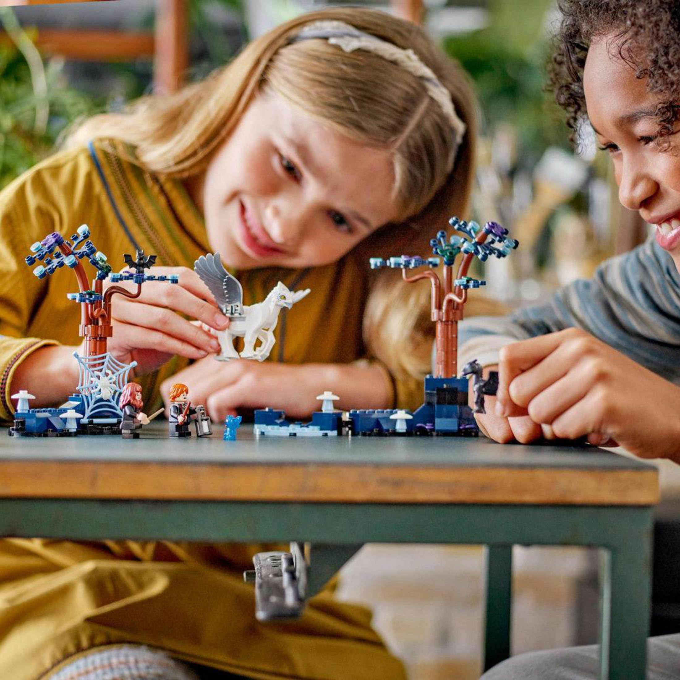 Zwei Kinder spielen mit einem Lego-Set. Ein Mädchen mit Stirnband zeigt einem Jungen ein weißes Pegasus.