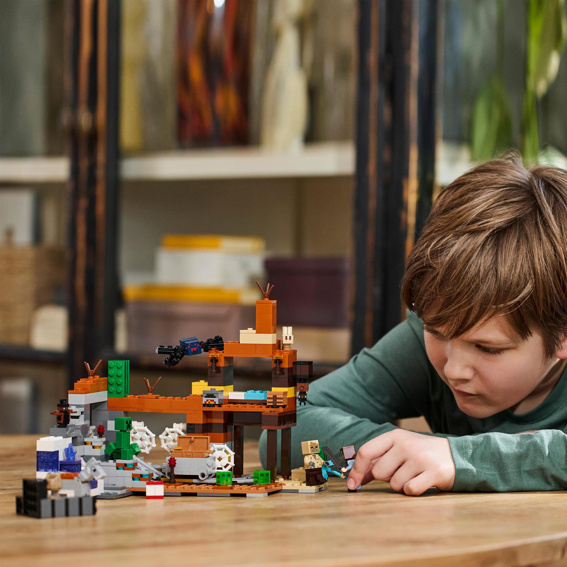 Een kind speelt met een Lego Minecraft set. De set toont een grotscène met figuren en details.