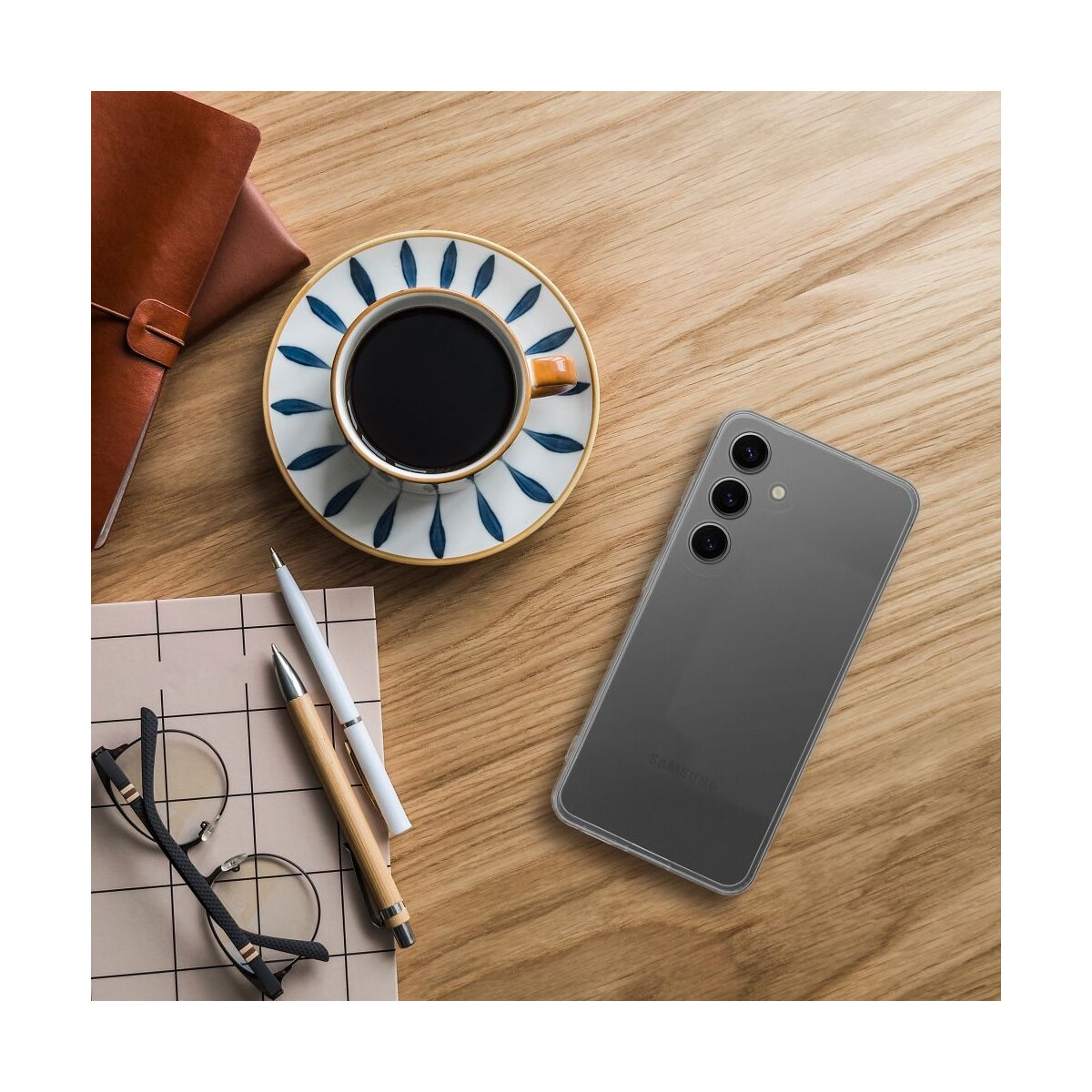 Un telefono su un tavolo di legno con una tazza di caffè, occhiali e penne. La scena suggerisce un ambiente di lavoro.