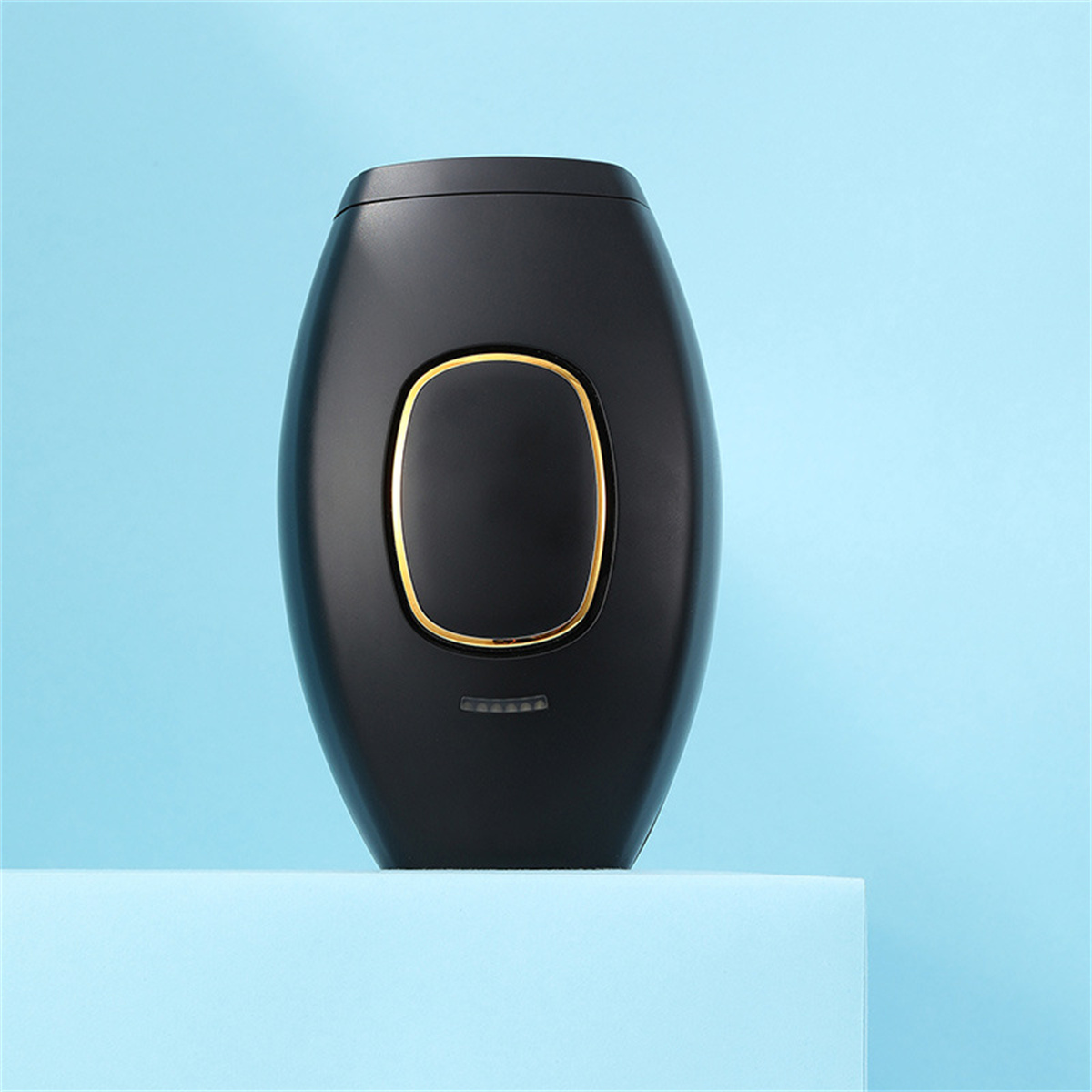 Schwarzes Haarentfernungsgerät mit goldenem Ring, auf blauer Oberfläche platziert.