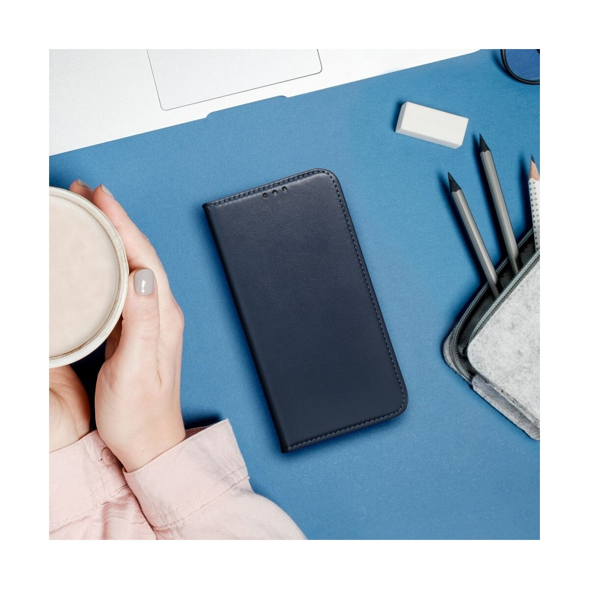 Mani con tazza e custodia del telefono su una superficie blu con matite, gomma e un laptop.