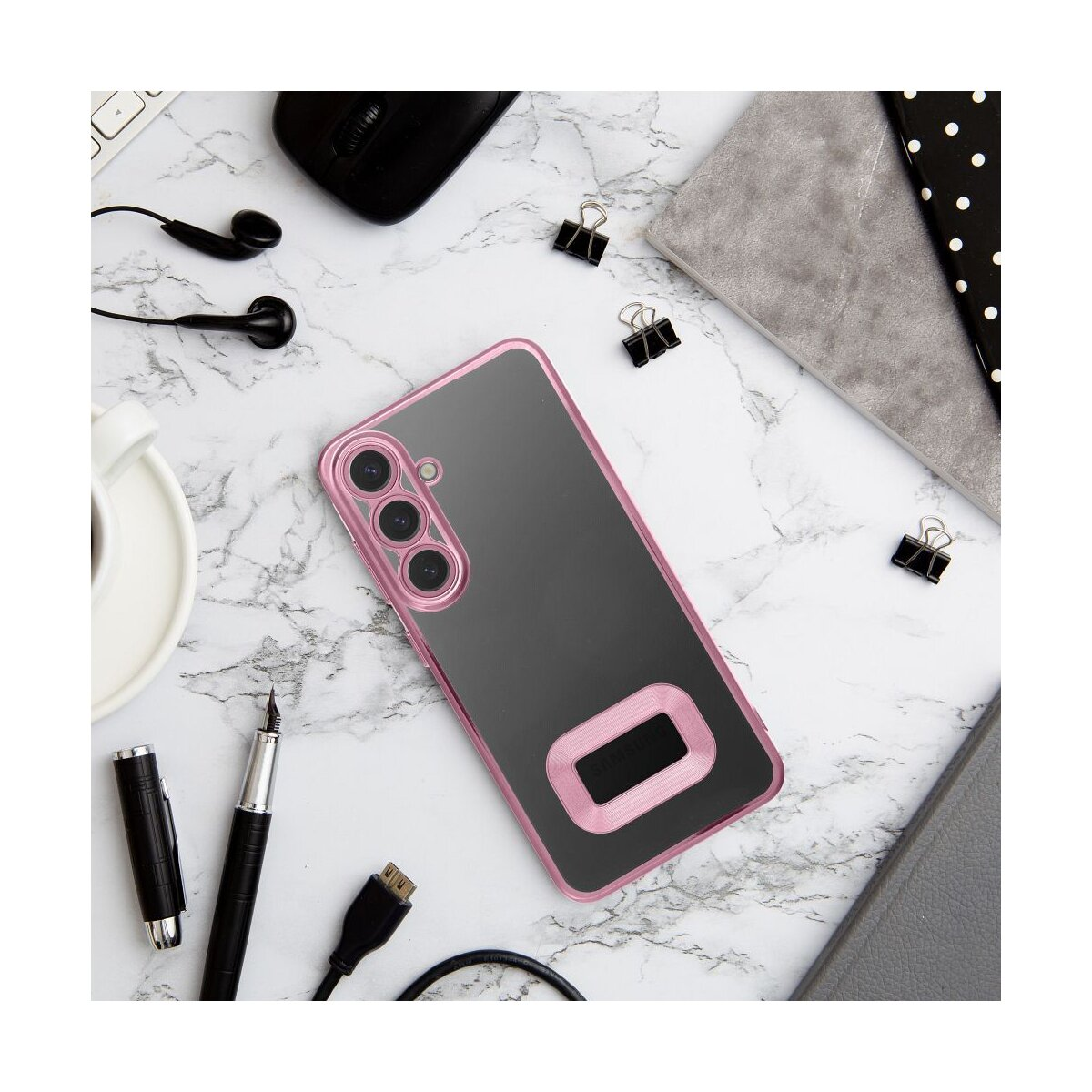 Custodia rosa per telefono su una superficie di marmo con accessori come penne e auricolari.