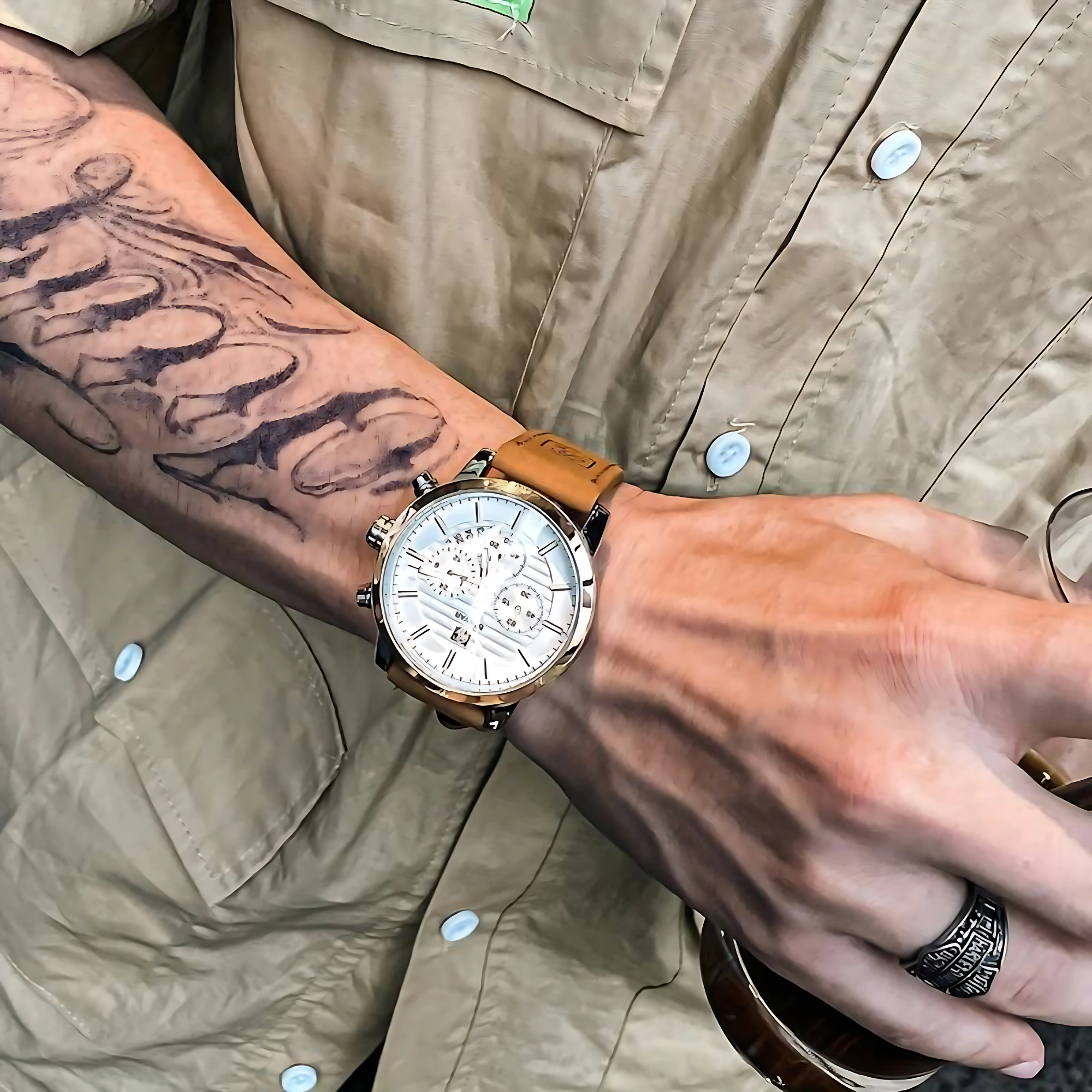 Arm einer Person mit Uhr, Tattoo und Ring, hält etwas.