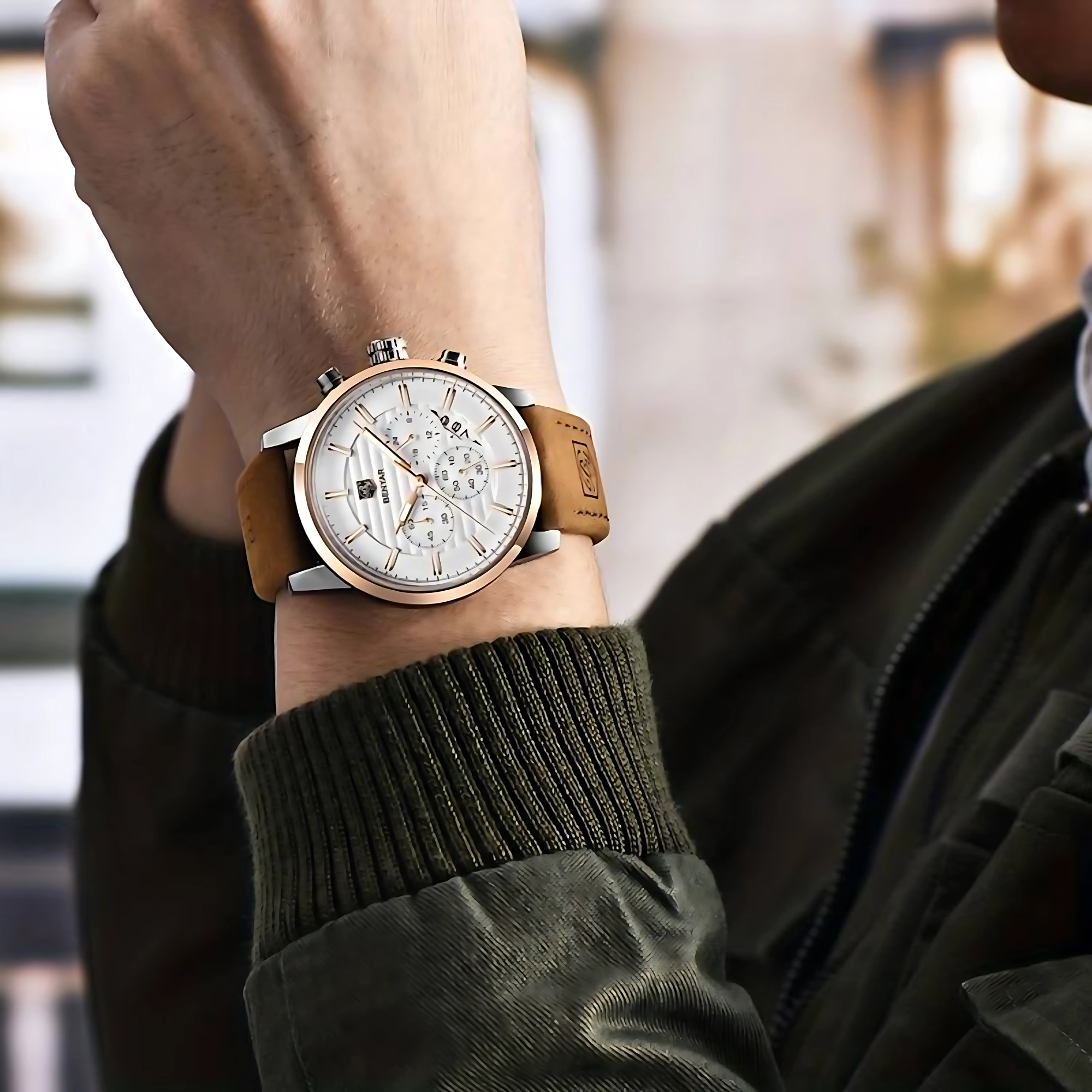 Mannes Handgelenk mit Uhr. Die Uhr hat ein silbernes Gehäuse, braunes Lederarmband und weißes Zifferblatt.