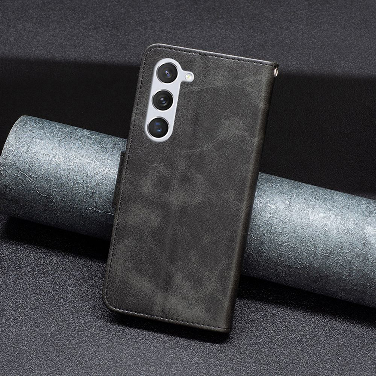 Donkergrijze leren telefoonhoes met een textuur en de camera van de telefoon zichtbaar.