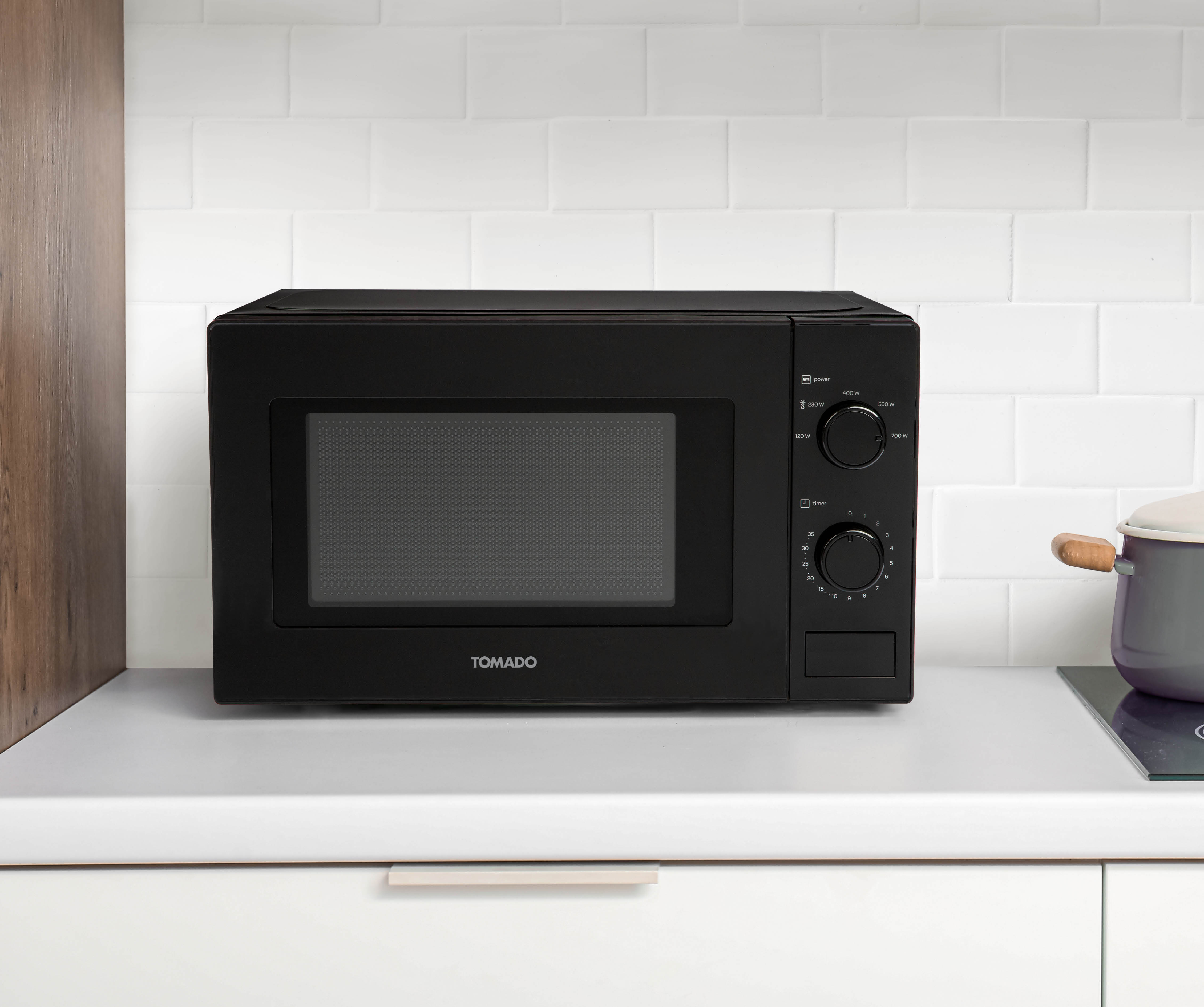 Black microwave on a white counter, with a white tiled wall backdrop.