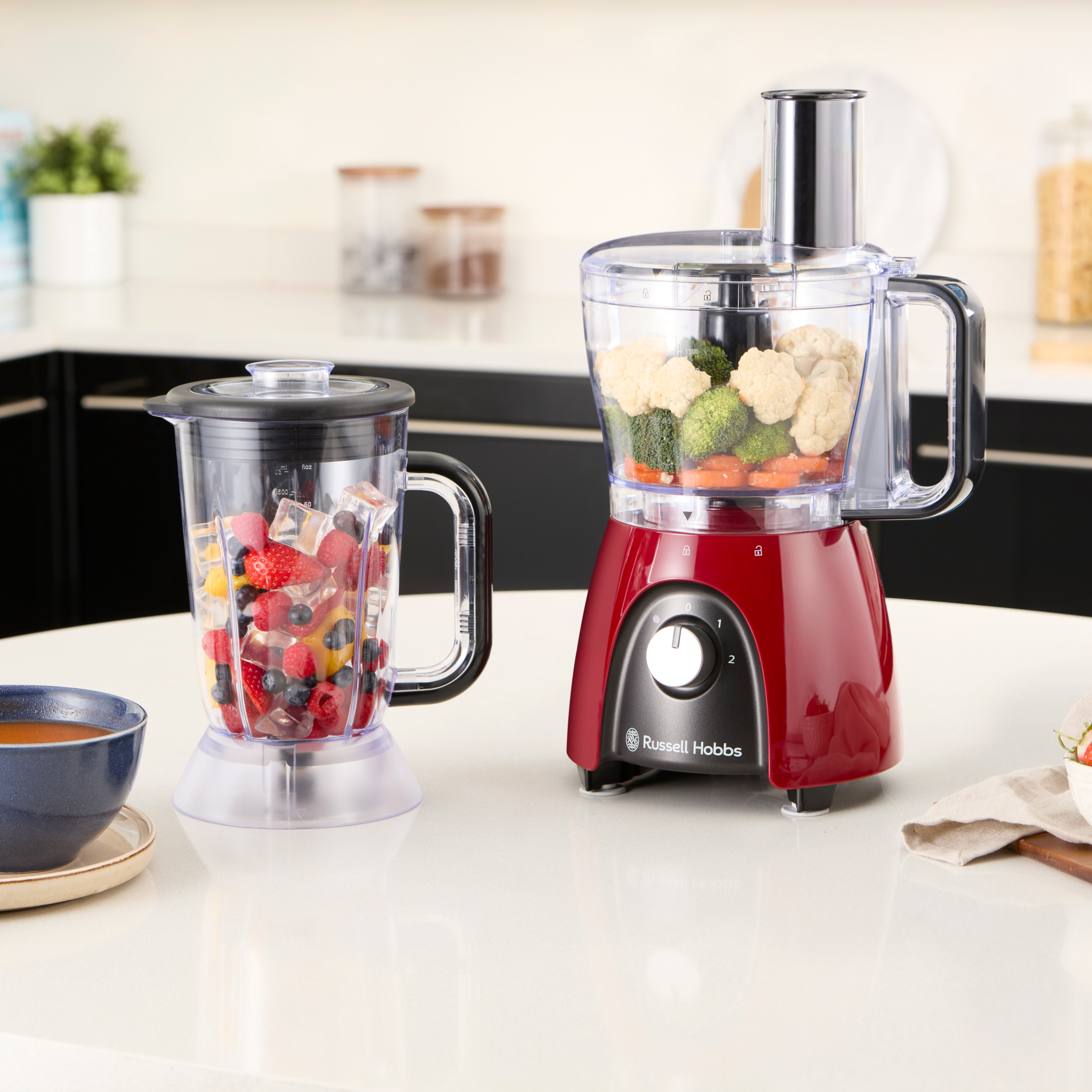 Un frullatore con ghiaccio e frutta e un robot da cucina con verdure. Entrambi sono rossi.