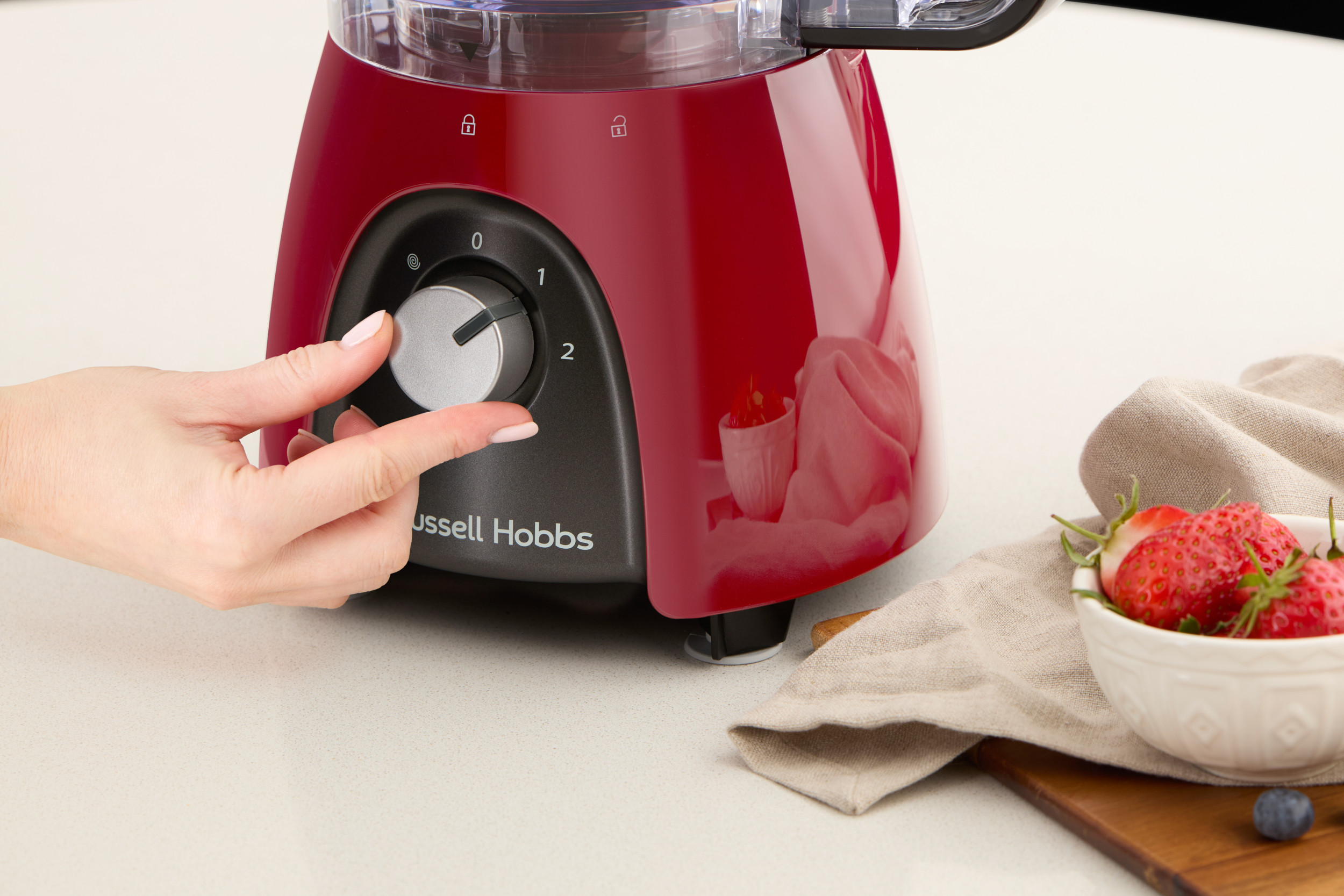 Mano che gira la manopola su un robot da cucina rosso, fragole vicine.