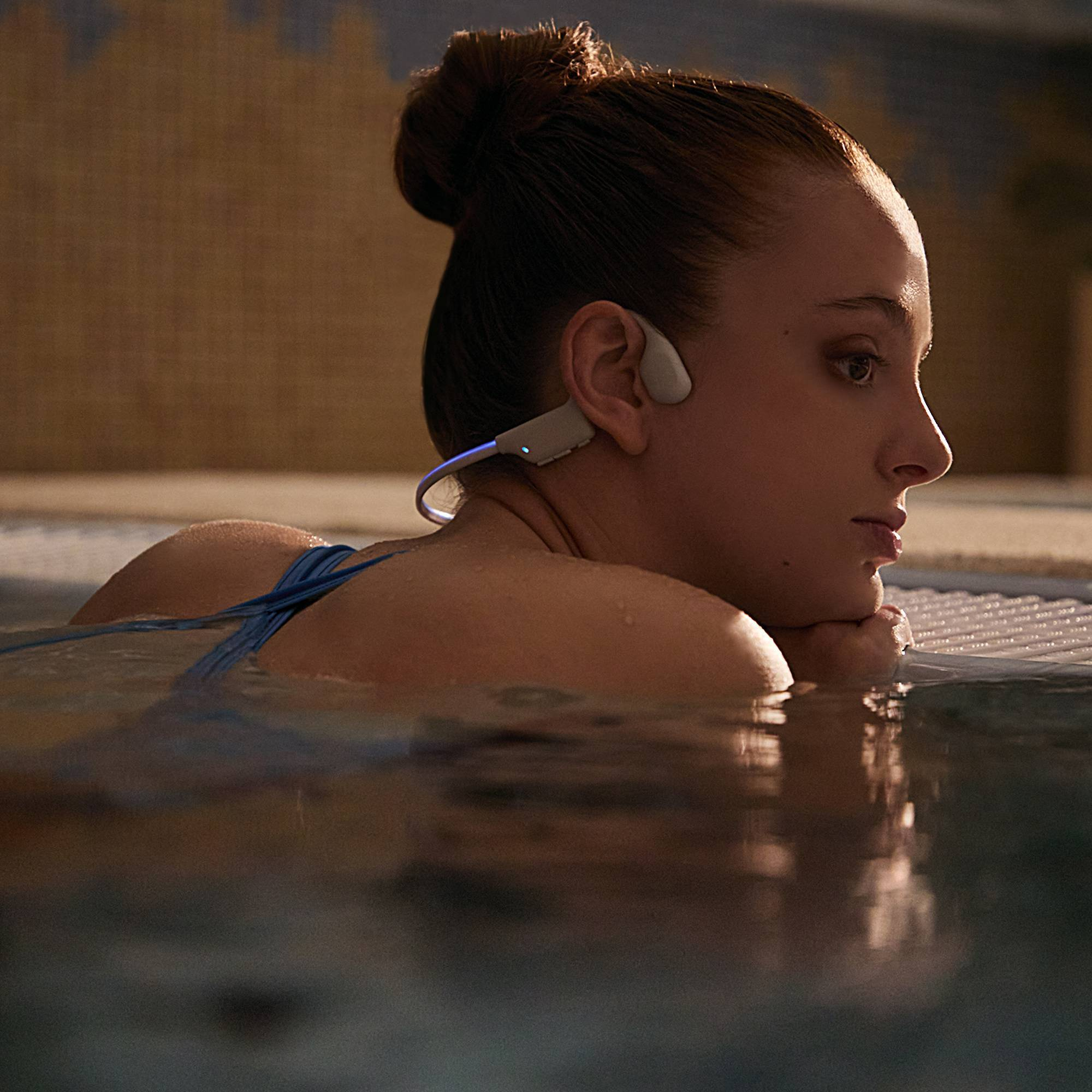 Una mujer en una piscina con auriculares de conducción ósea. Se relaja en el agua.