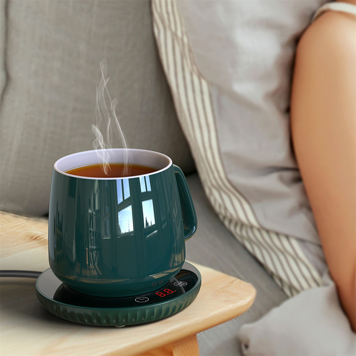 Eine Tasse auf einem Wärmer, aus dem Dampf aufsteigt. Die Tasse ist dunkelgrün. Der Wärmer ist schwarz. Der Hintergrund ist grau.