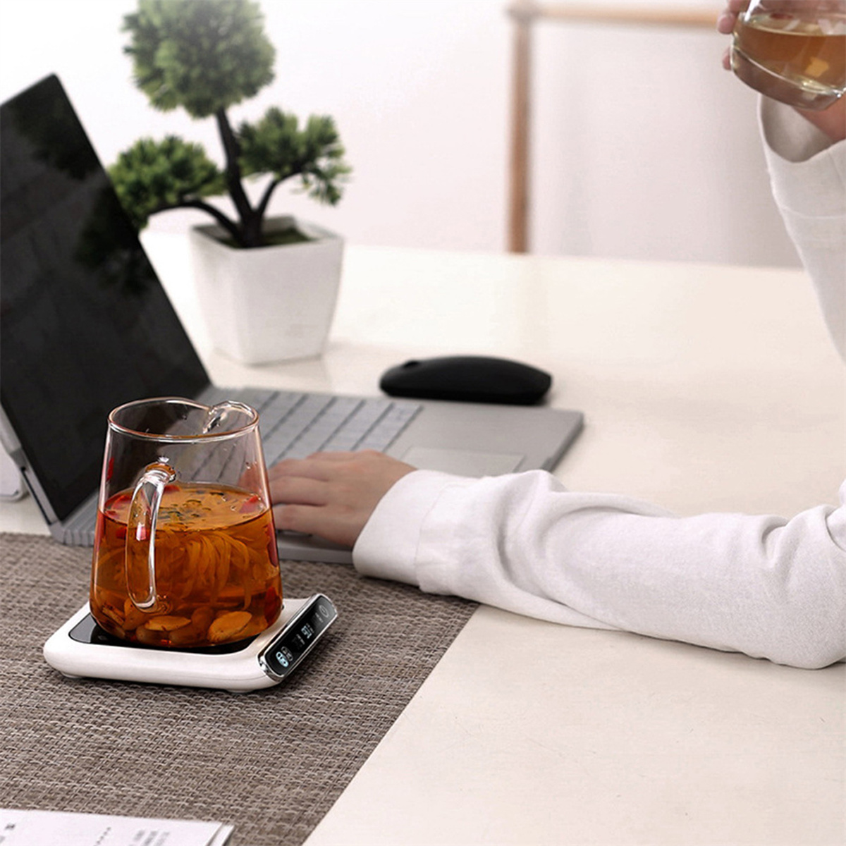 Eine Person benutzt einen Laptop mit einem Glasbecher auf einem Wärmer.