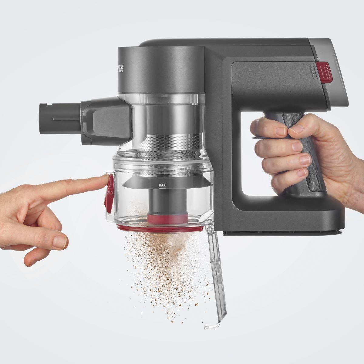 De hand van een persoon bedient een grijze en transparante handheld stofzuiger, waarbij stofdeeltjes worden uitgestoten.