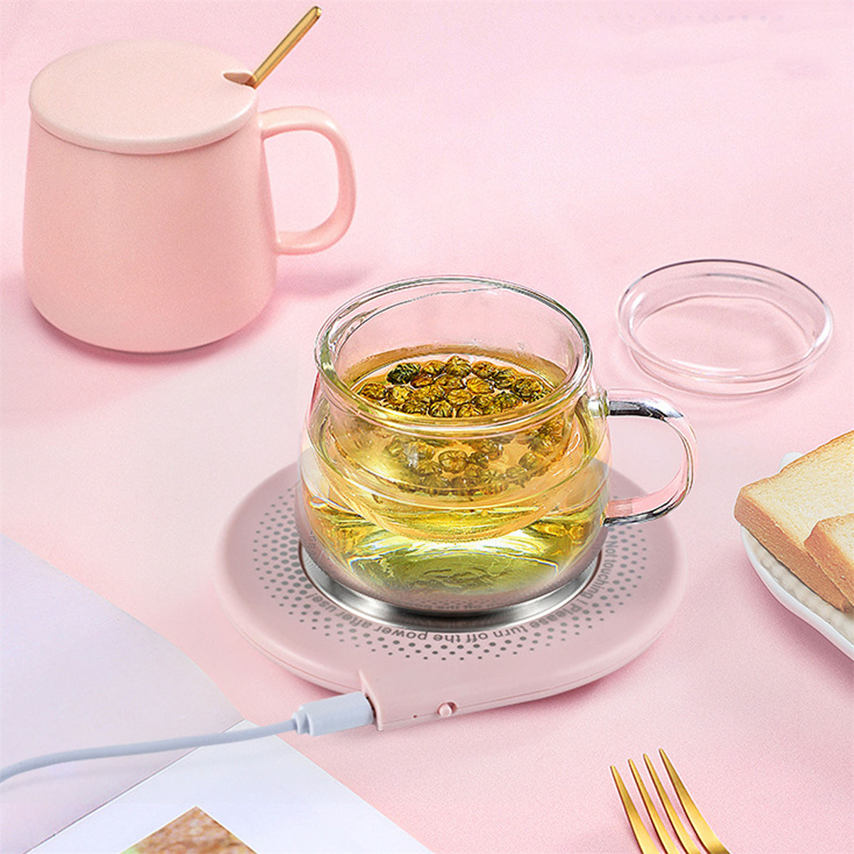 Eine rosa Tasse mit Deckel und Löffel, ein Glas Tee auf einem rosa Untersetzer und eine Scheibe Brot.