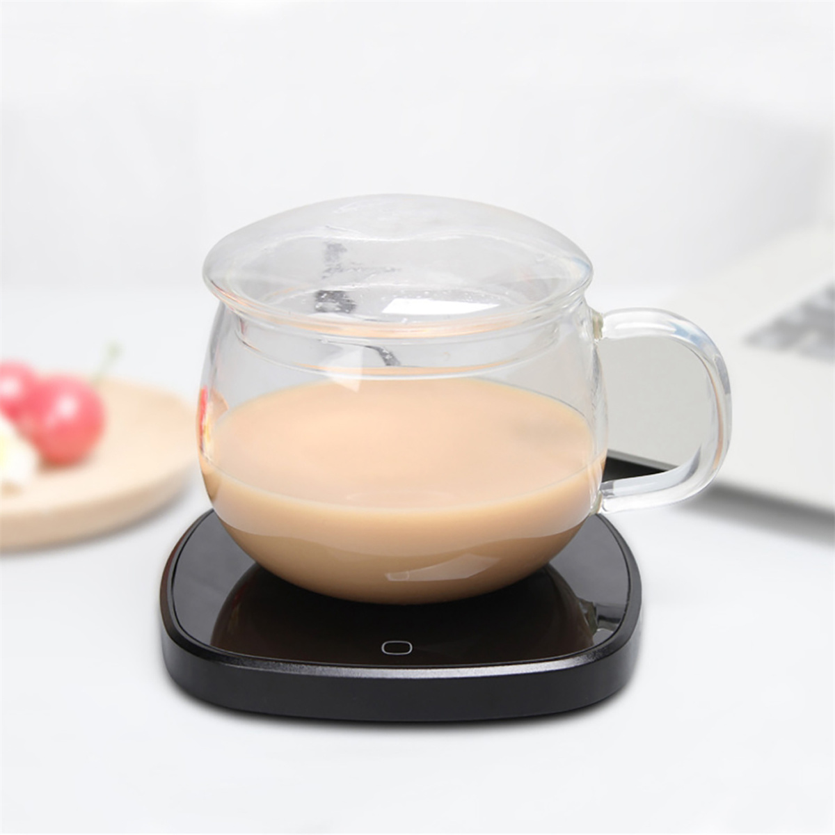 Glasbecher mit Tee auf schwarzem Wärmer, weiße Oberfläche, verschwommener Hintergrund.