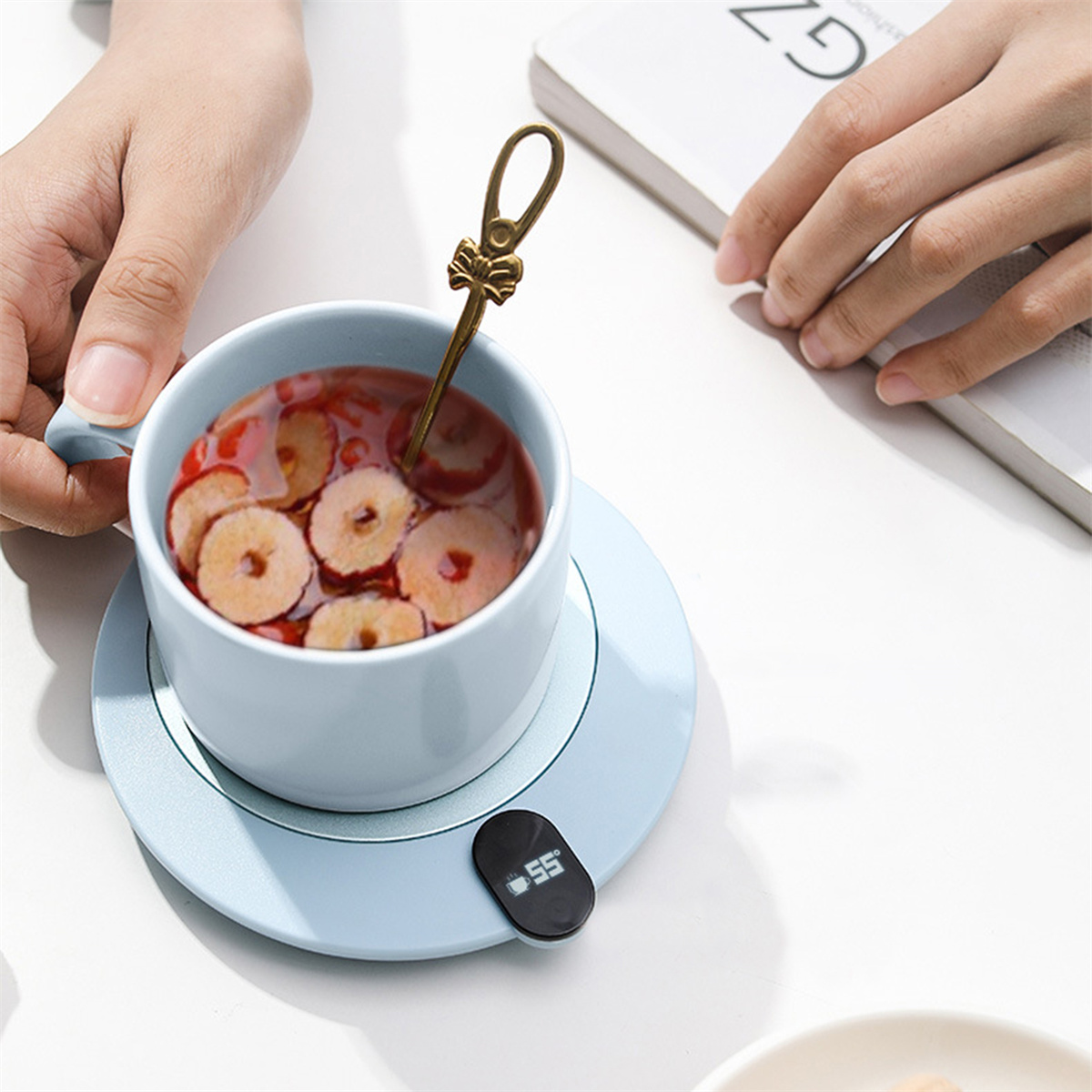 Eine blaue Tasse mit Tee und Früchten steht auf einem hellblauen Wärmer mit digitaler Anzeige von 55.