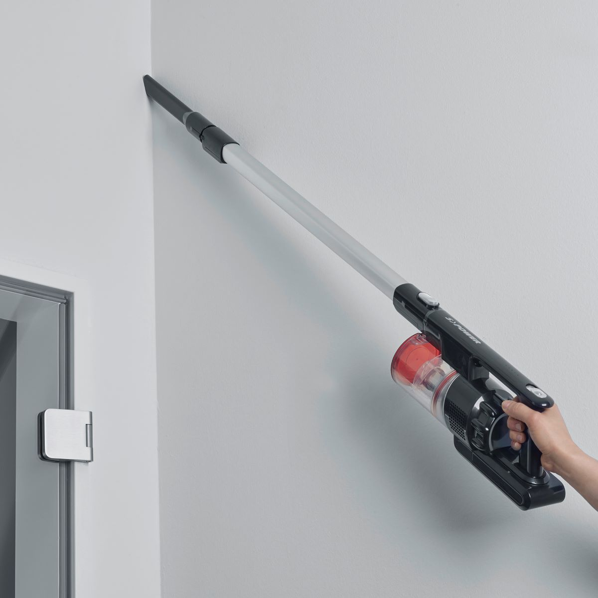 Una persona usando una aspiradora negra y roja en una pared blanca cerca de un marco de puerta.