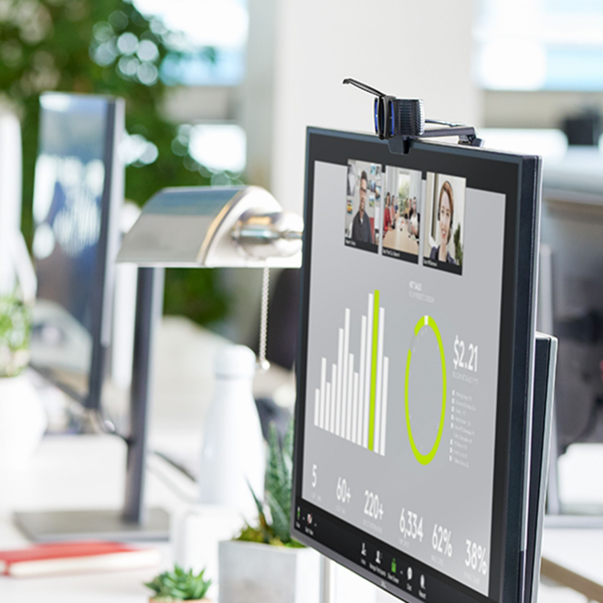 Monitor wyświetla wideokonferencję. Lampa po lewej stronie. Biurko w jasnym biurze.