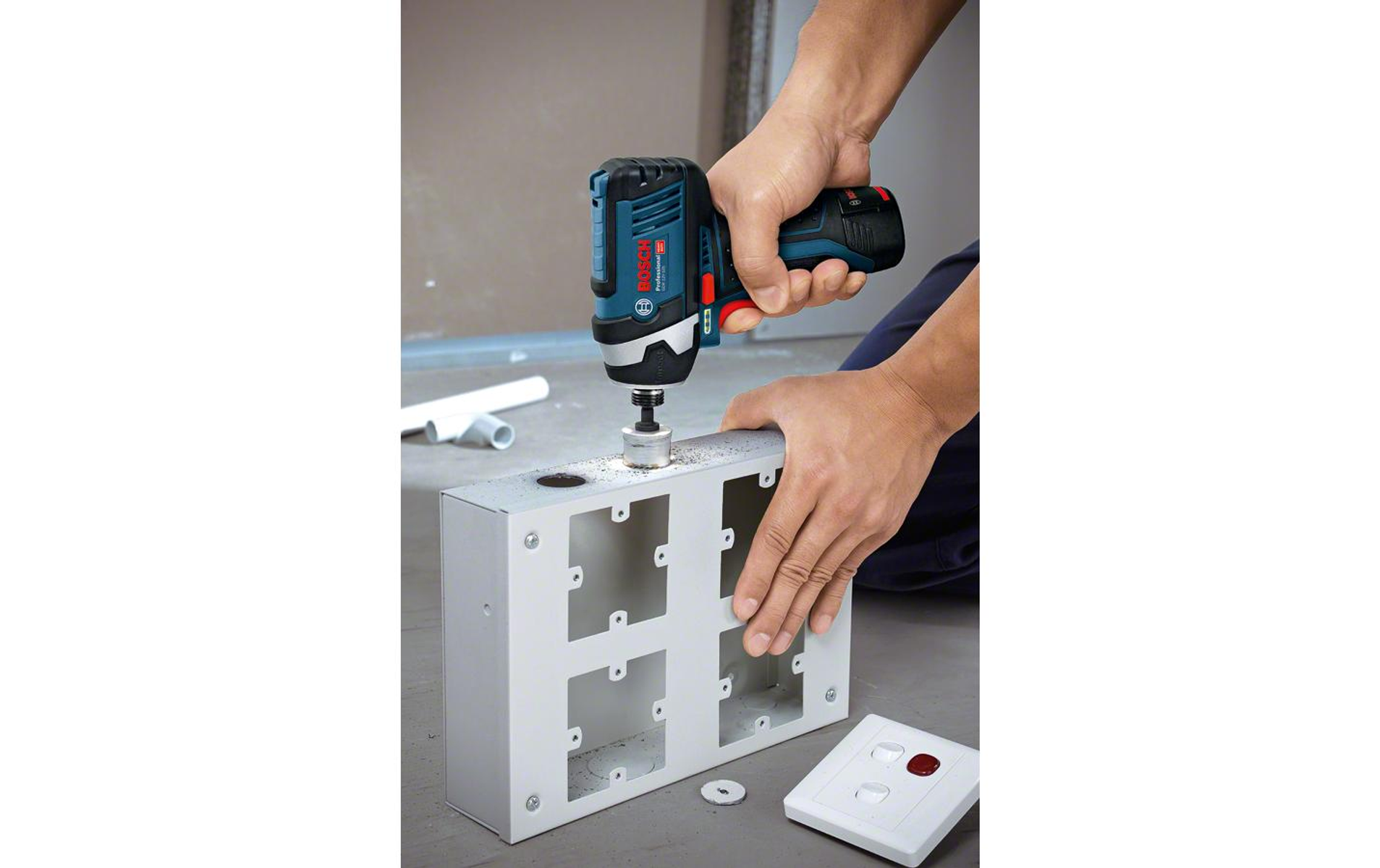 Osoba wierci otwór w metalowej skrzynce za pomocą niebiesko-czarnej wiertarki.