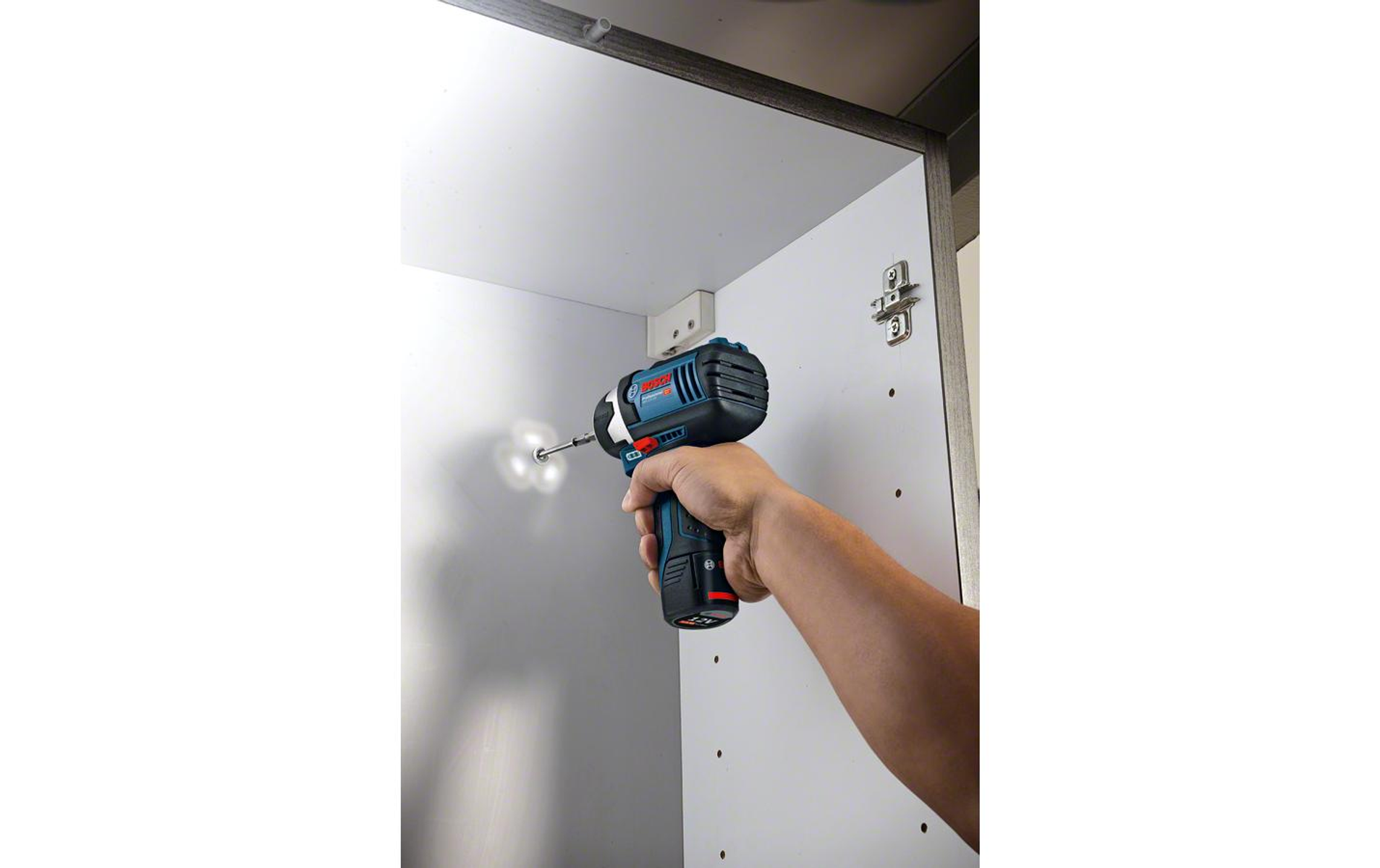 Ręka używająca niebiesko-czarnej wiertarki do wkręcania w białą szafkę.