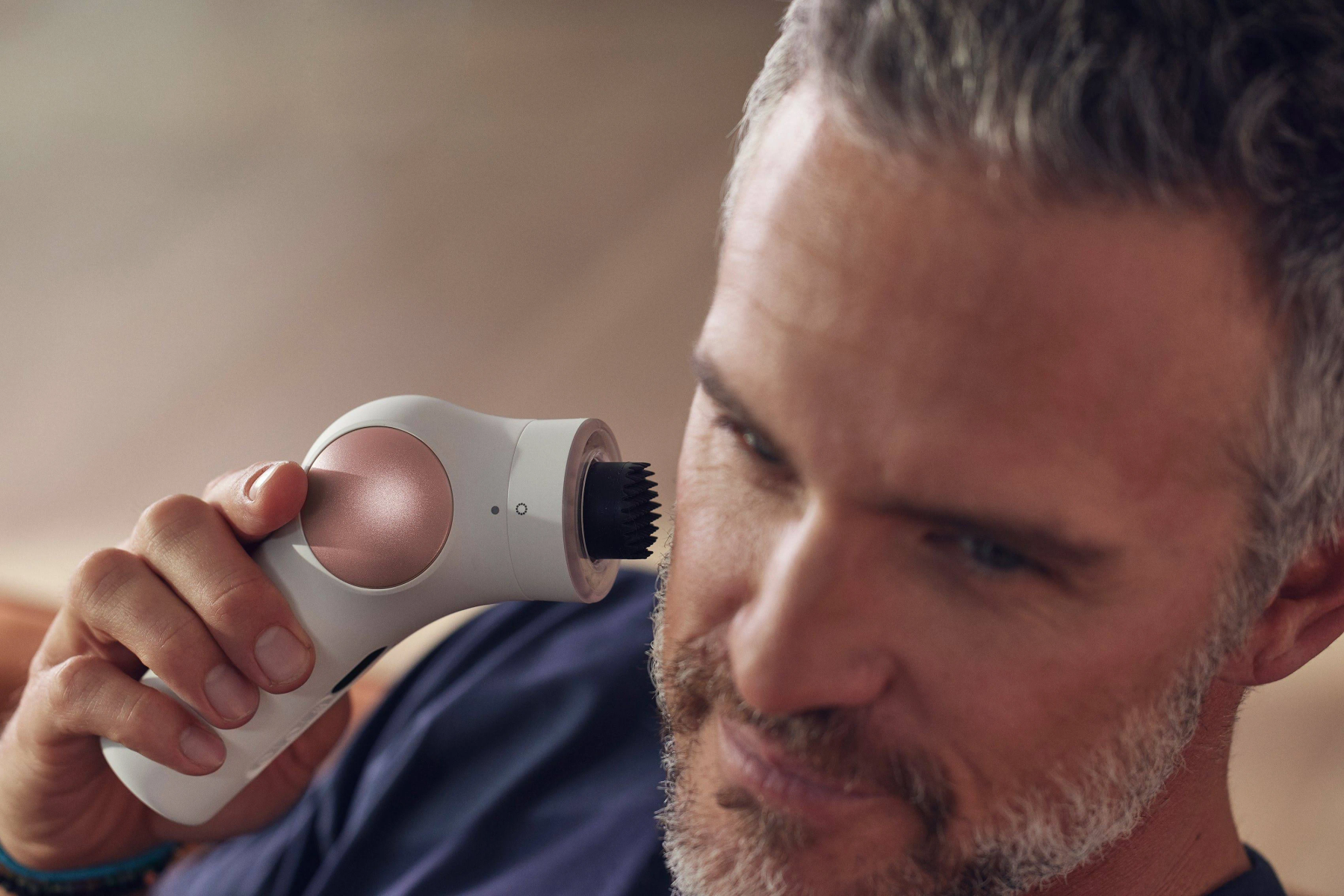 Hombre usando un dispositivo de limpieza facial. El dispositivo se sostiene en su mejilla.