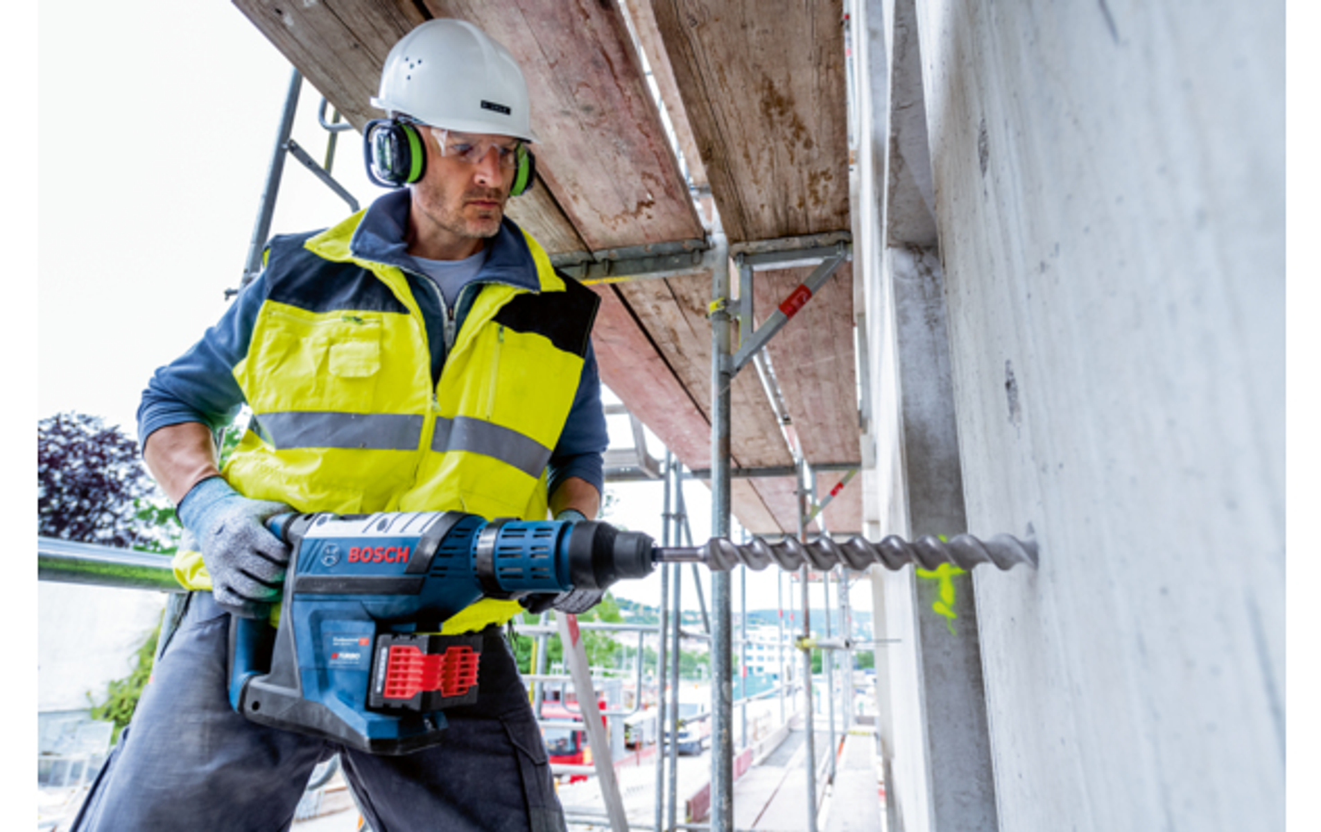 Trabajador de la construcción taladrando una pared de hormigón con una herramienta eléctrica grande, con equipo de seguridad.