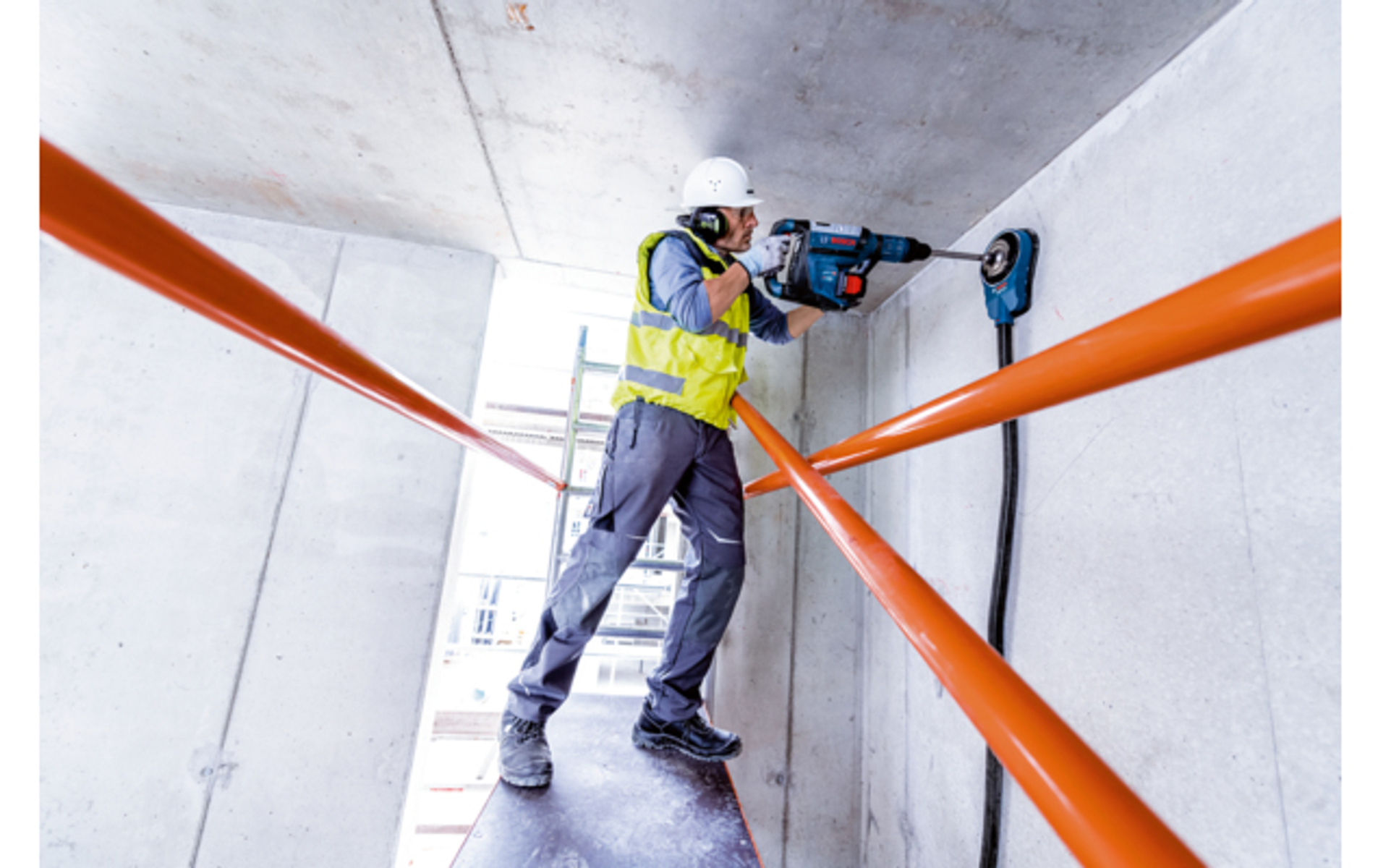Un trabajador de la construcción perforando una pared, con chaleco y casco.