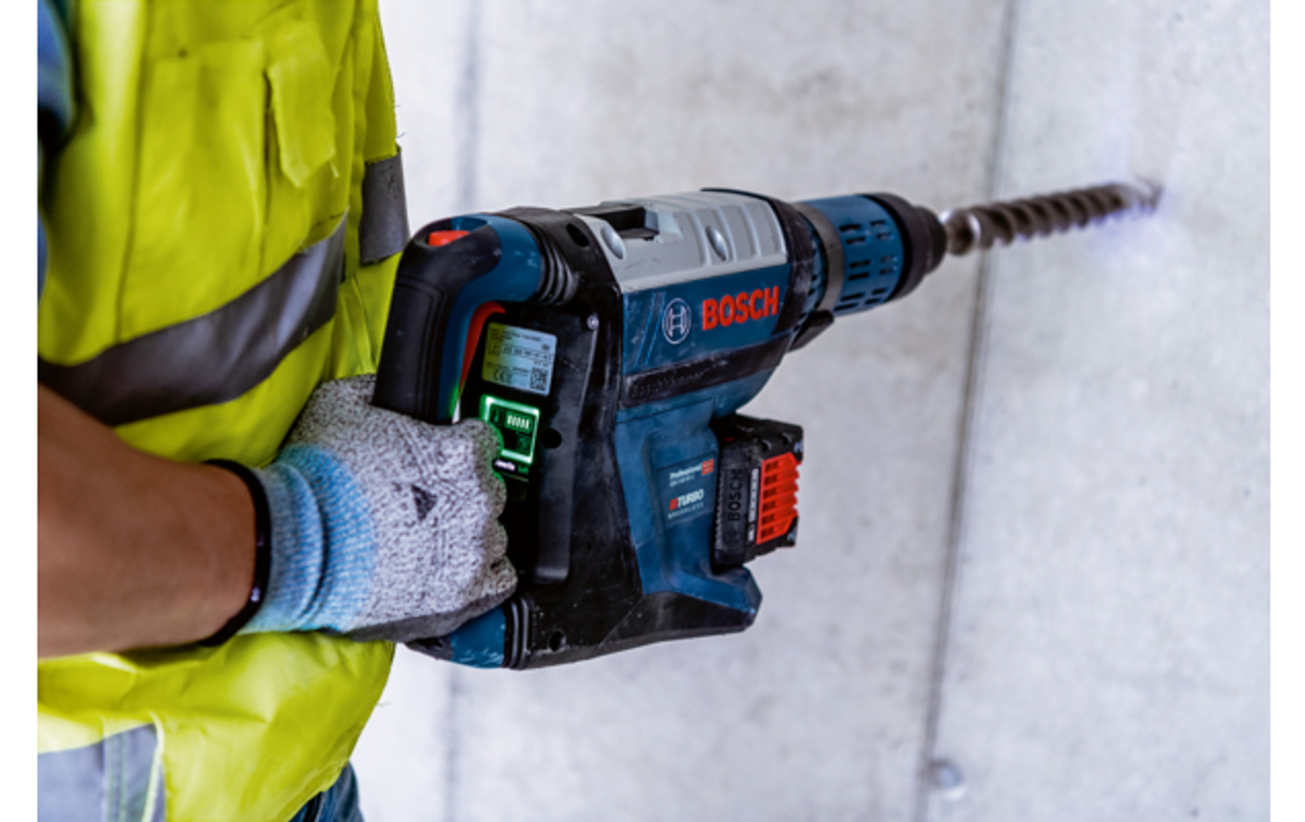 Un trabajador de la construcción usando un taladro Bosch para perforar una pared de concreto.