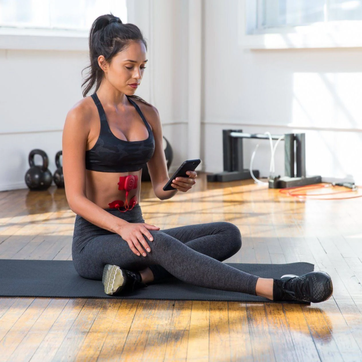 Mujer sentada, usando un teléfono, con un diagrama de órganos internos superpuesto en su torso, en un gimnasio.