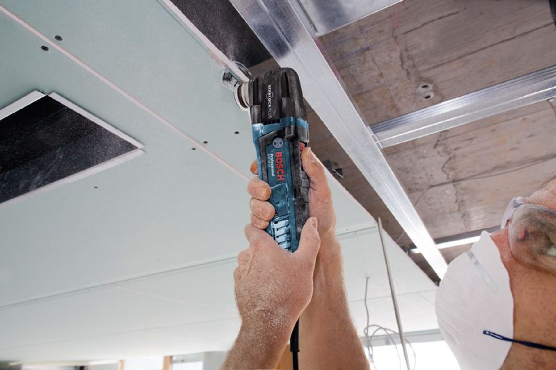Mann benutzt Bosch Multi-Tool an der Decke. Das Werkzeug ist blau und schwarz.