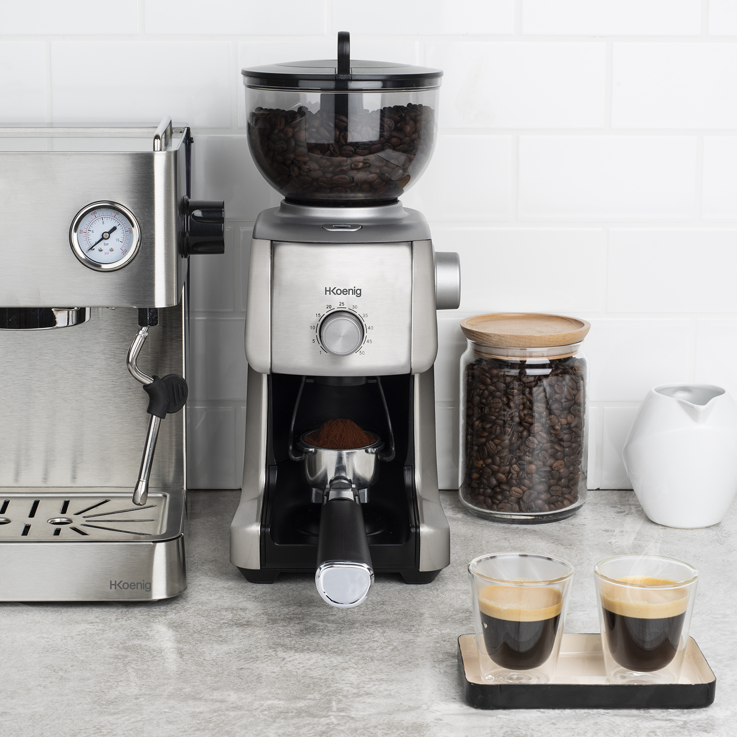 Macchina da caffè, macinacaffè, tazze espresso con chicchi e lattiera sul bancone.