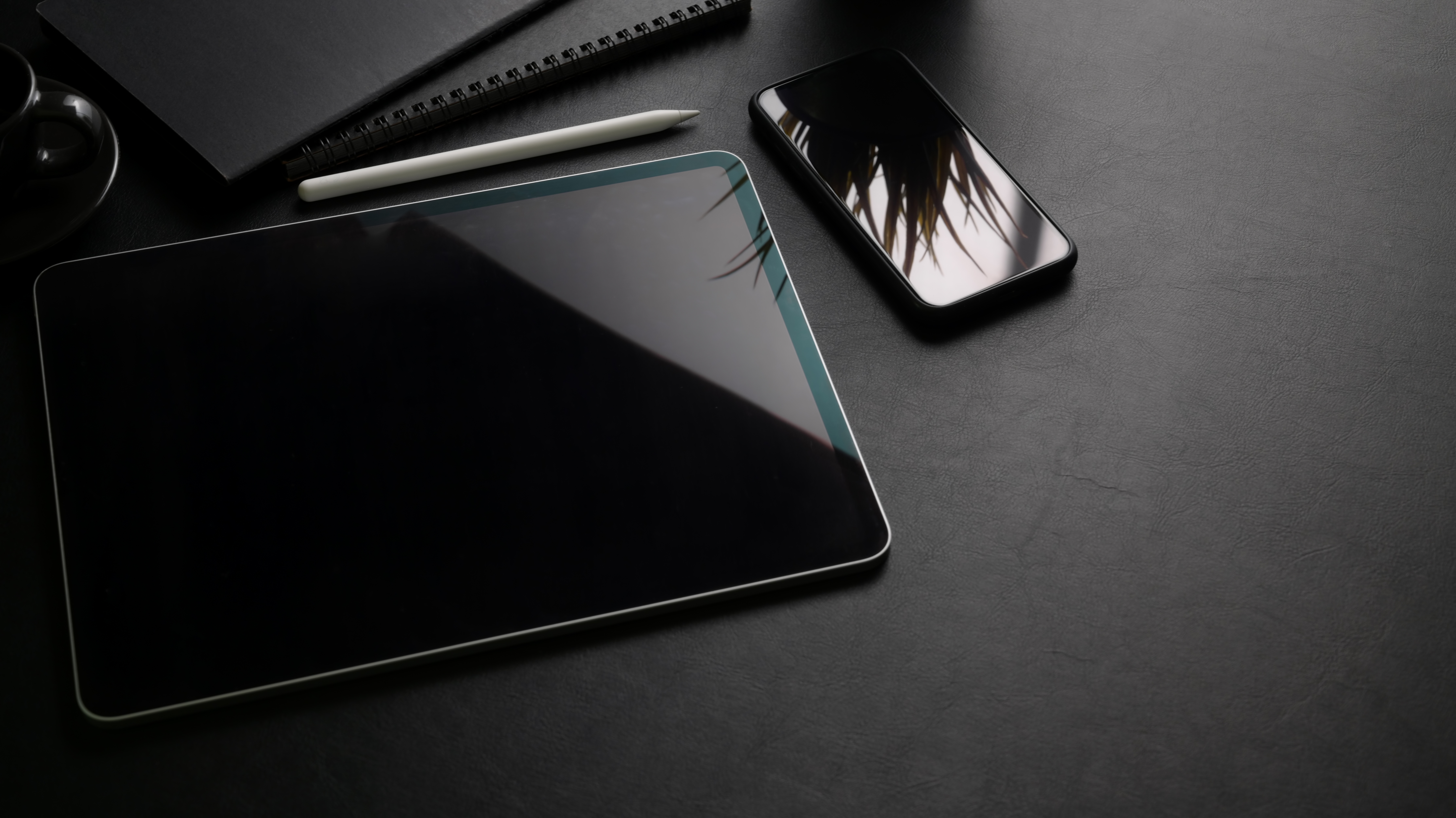 Tablet e telefono su una superficie scura. Una penna e un blocco note sono anch'essi sulla superficie.