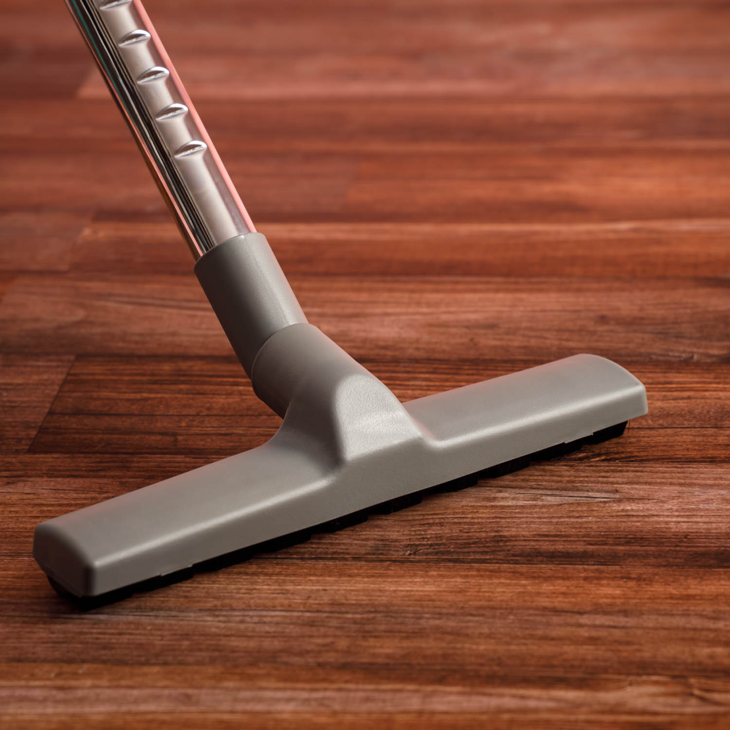 Głowica odkurzacza na drewnianej podłodze. Głowica jest szara, ze szczotką na spodzie.