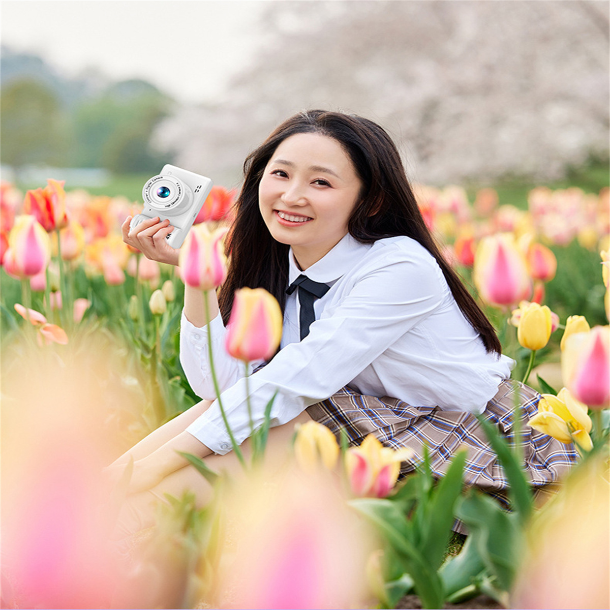Lachende Frau hält eine weiße Kamera in einem Tulpenfeld, sonniger Tag.