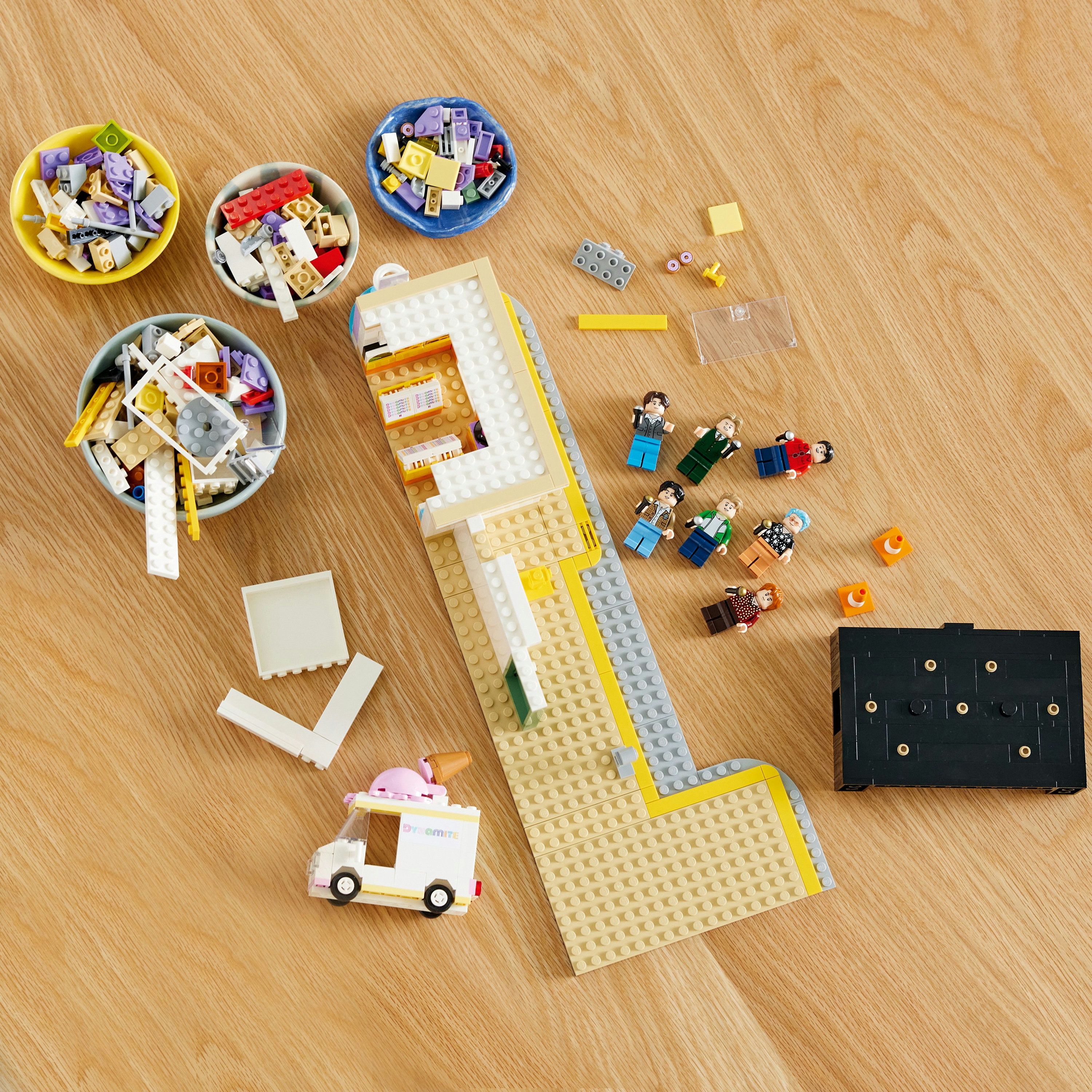 LEGO set parçaları, minifigürler ve bir yemek kamyonu dahil, ahşap bir yüzeyde düzenlenmiş.