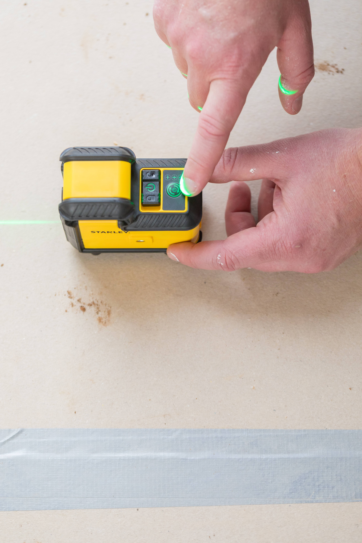 Ręka osoby naciskająca zielony przycisk na żółto-czarnym poziomnicy laserowym.