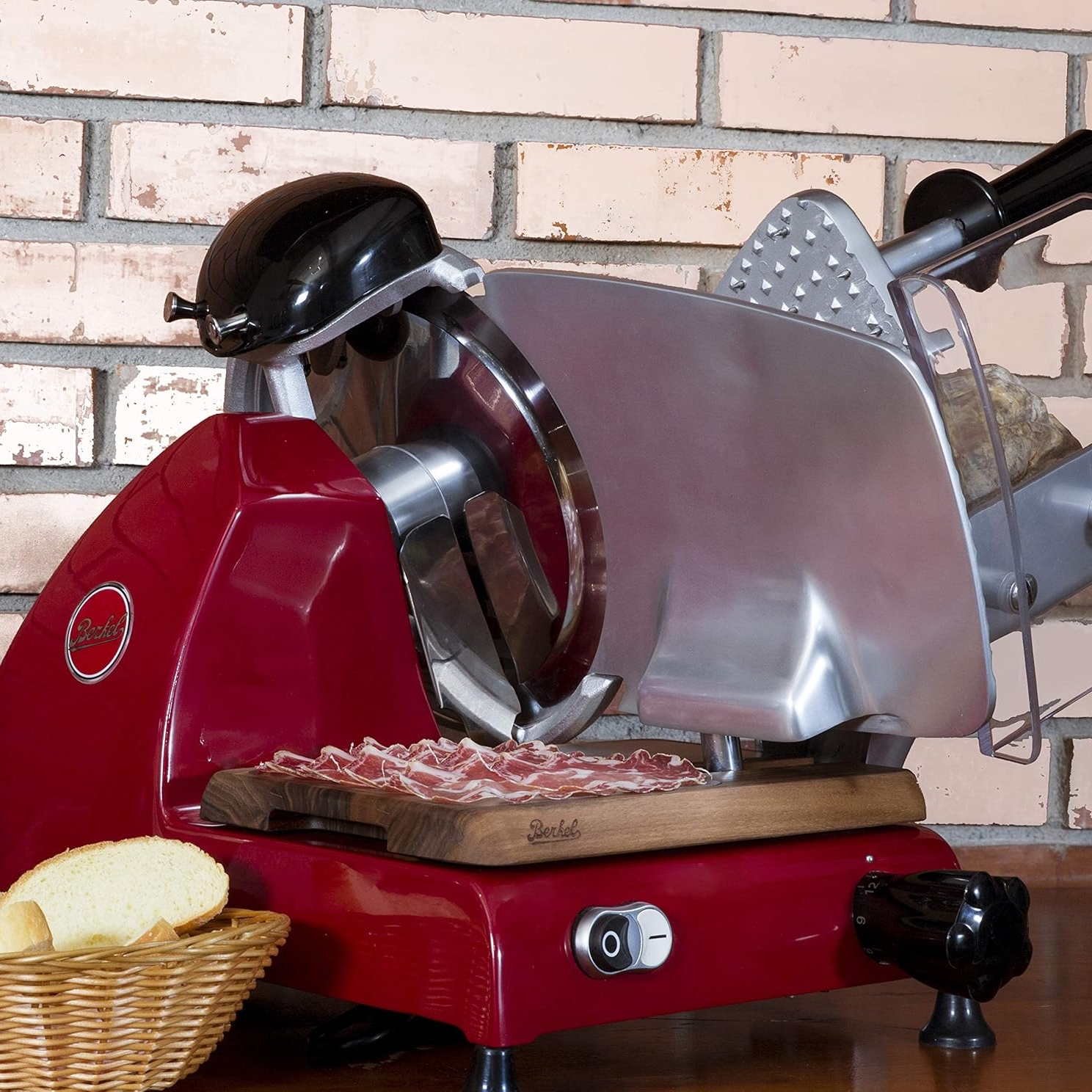 Affettatrice Berkel rossa, con tagliere in legno, carne affettata, pane e cestino.