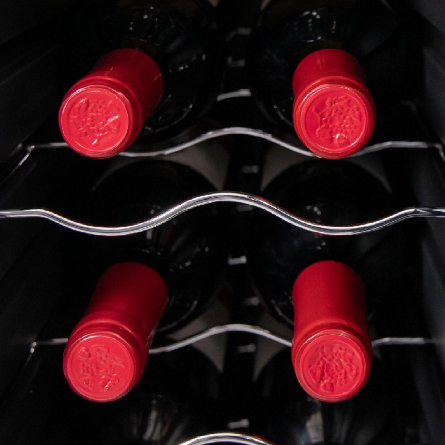 Zbliżenie na butelki wina w chłodziarce. Butelki mają czerwone zakrętki. Czarne wnętrze chłodziarki.