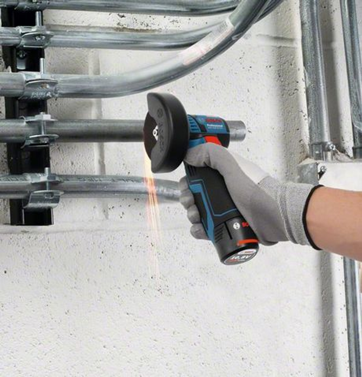 Osoba używająca niebiesko-czarnej szlifierki kątowej na metalowych rurach. Widoczne iskry.
