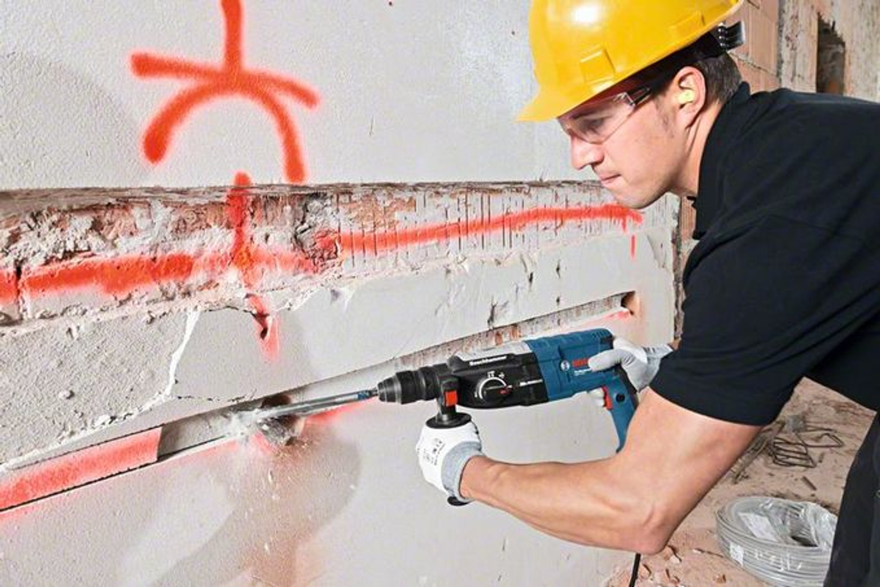 Mężczyzna używa młota udarowego Bosch na ścianie, w sprzęcie ochronnym.