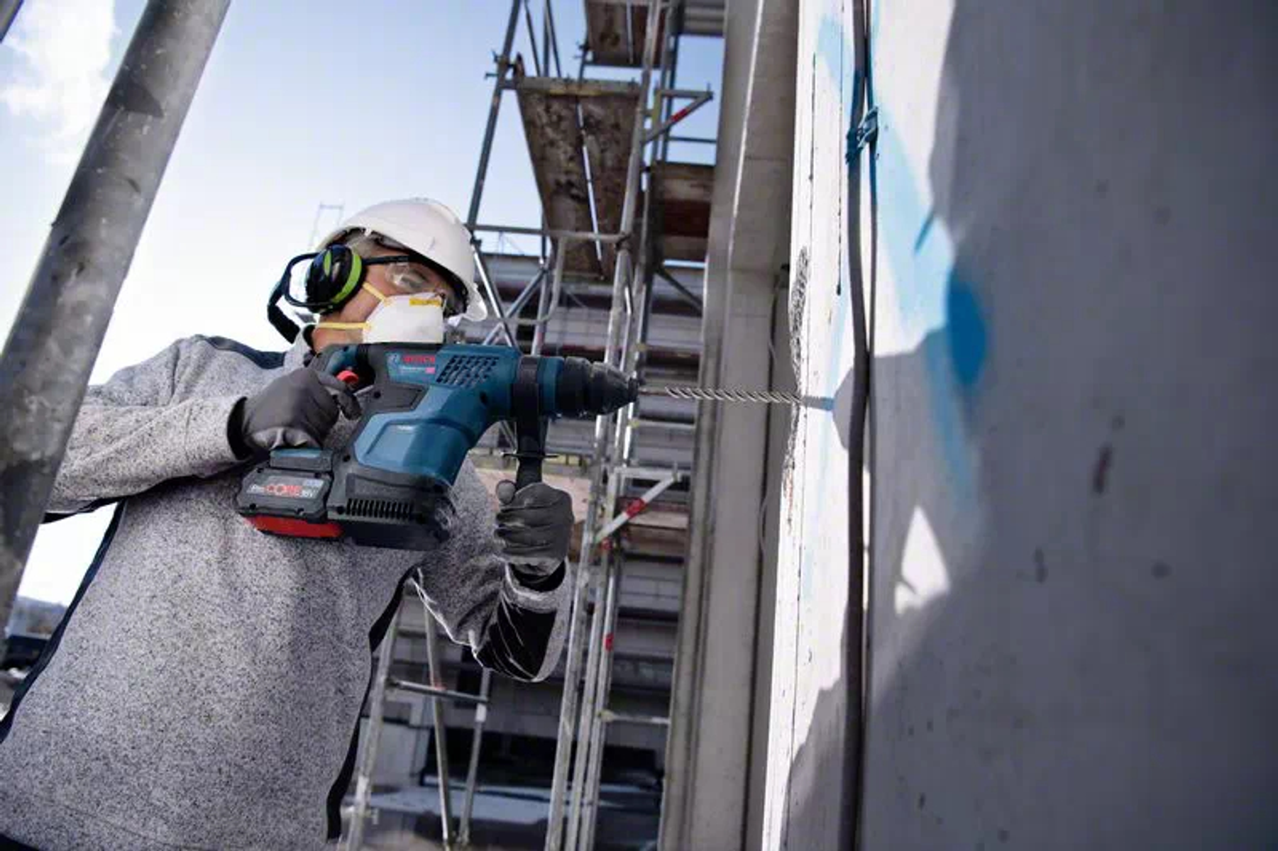 Osoba używająca niebiesko-czarnej wiertarki na betonowej ścianie.