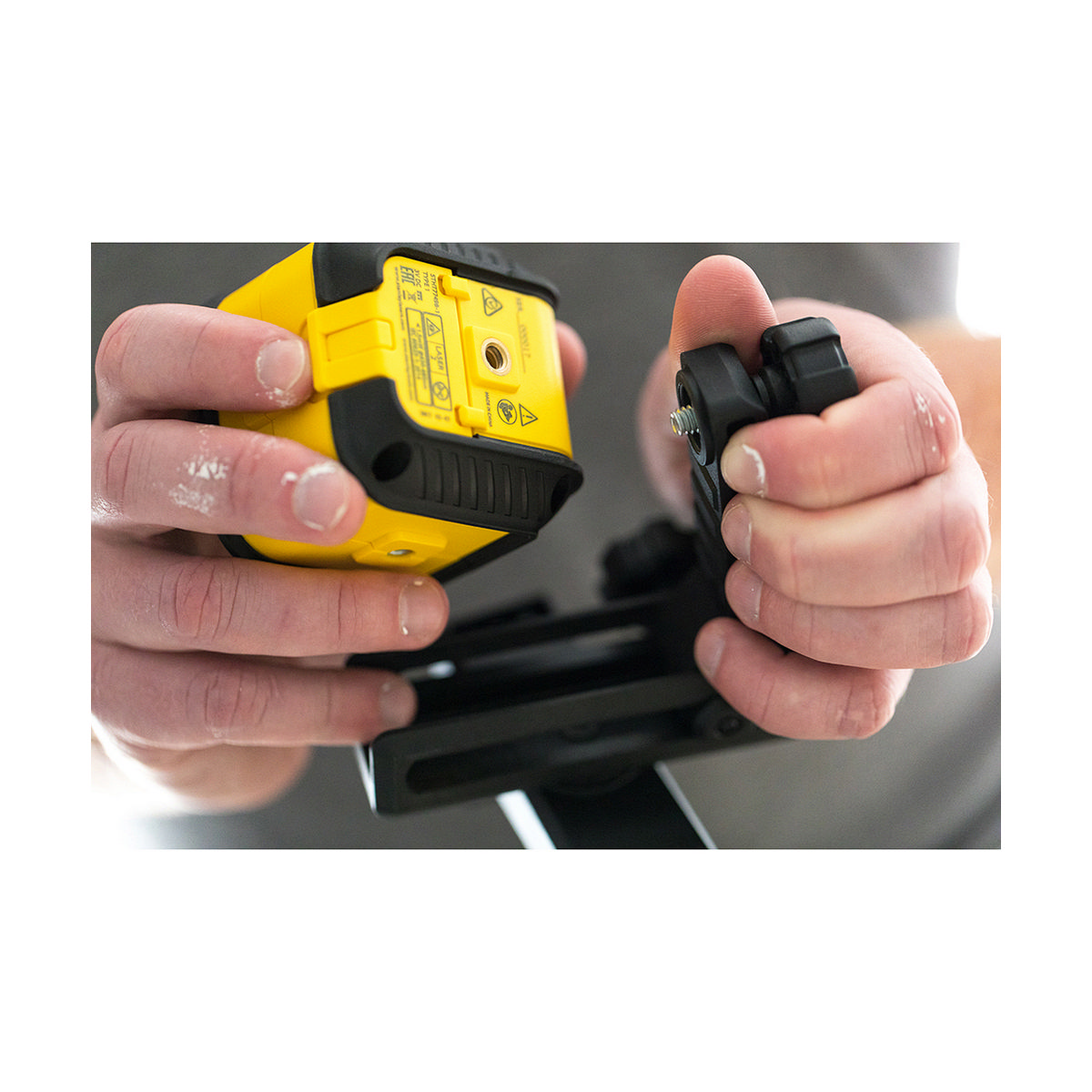 Dłonie trzymające żółtą poziomnicę z czarnymi i szarymi elementami.