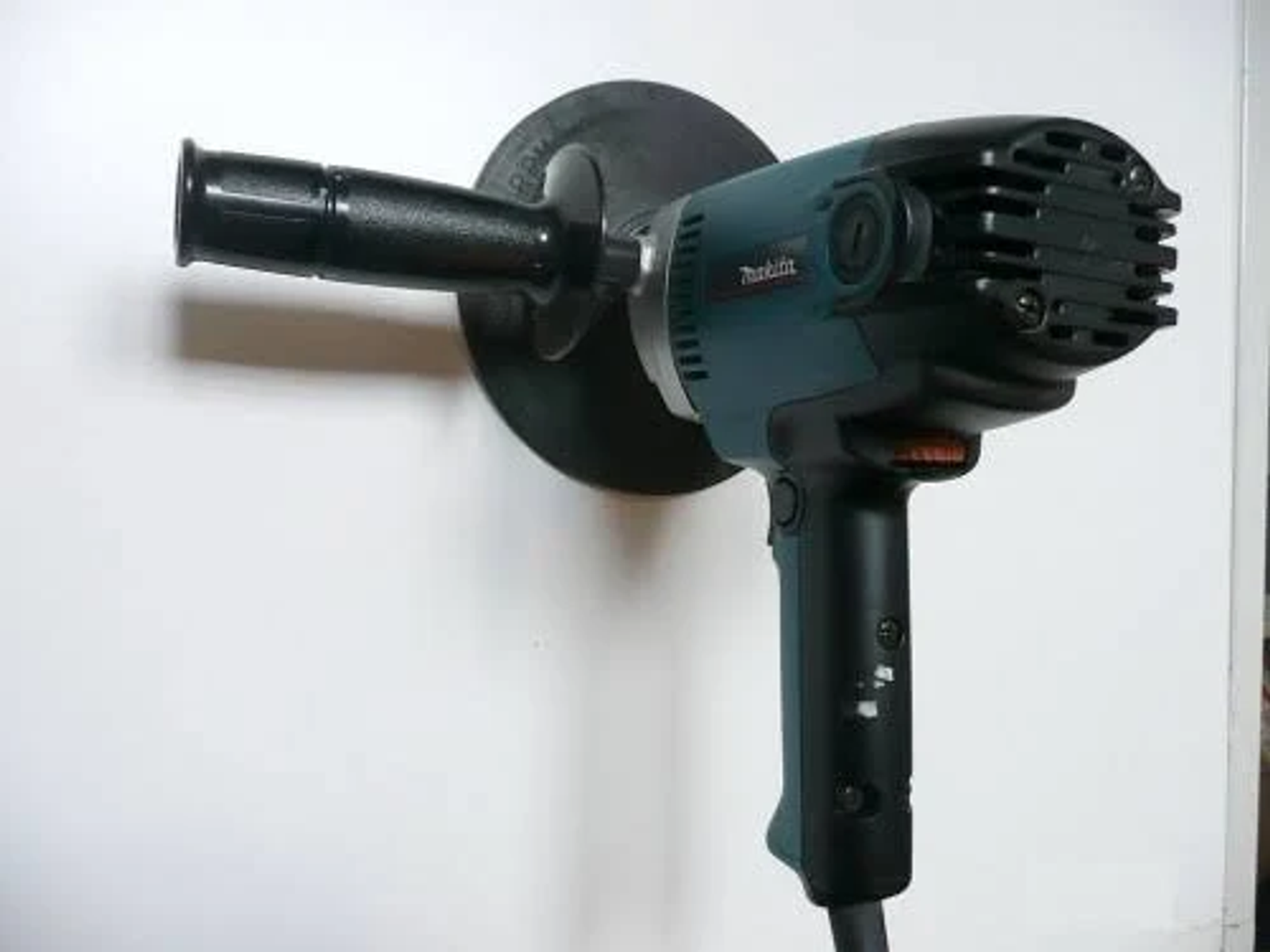 Una pulidora Makita negra y turquesa sobre un fondo blanco, con un mango negro.