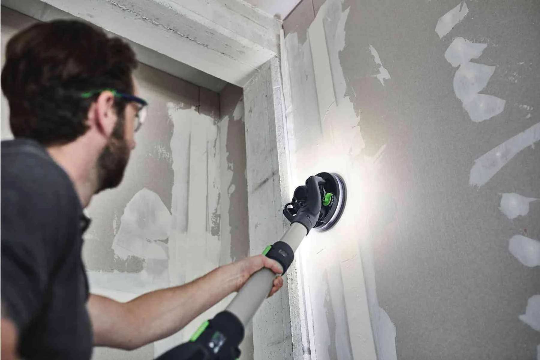 Un hombre usando una lijadora de pared en una pared de yeso en un entorno de construcción.